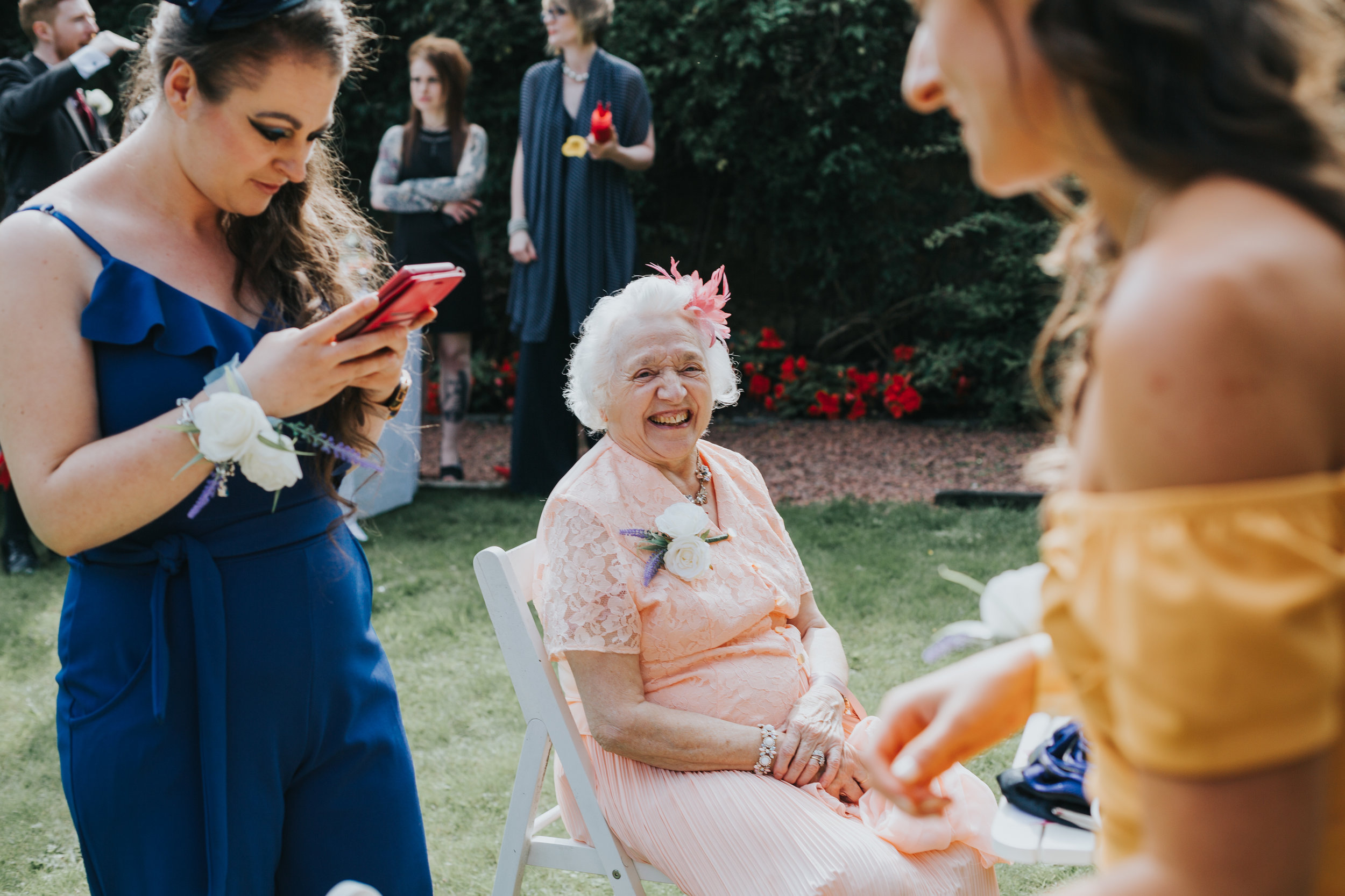 Grandma sits laughing surrounded by young ones on their phones. 