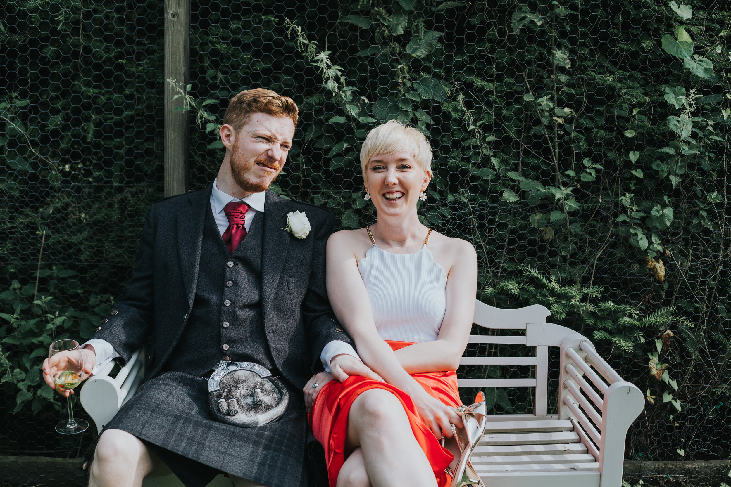 Bride and groom chill on a bench together.