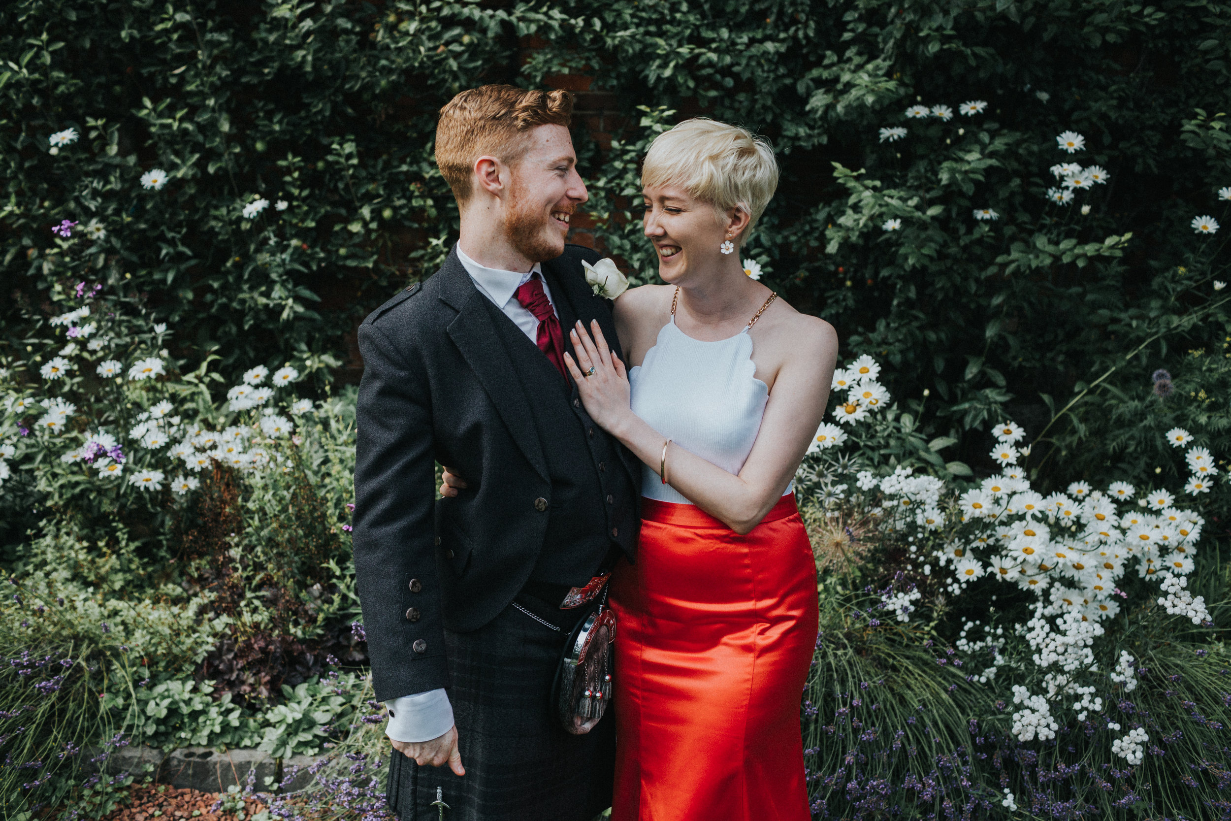 Bride and groom stand laughing together in the walled garden at Shotton Grange. 