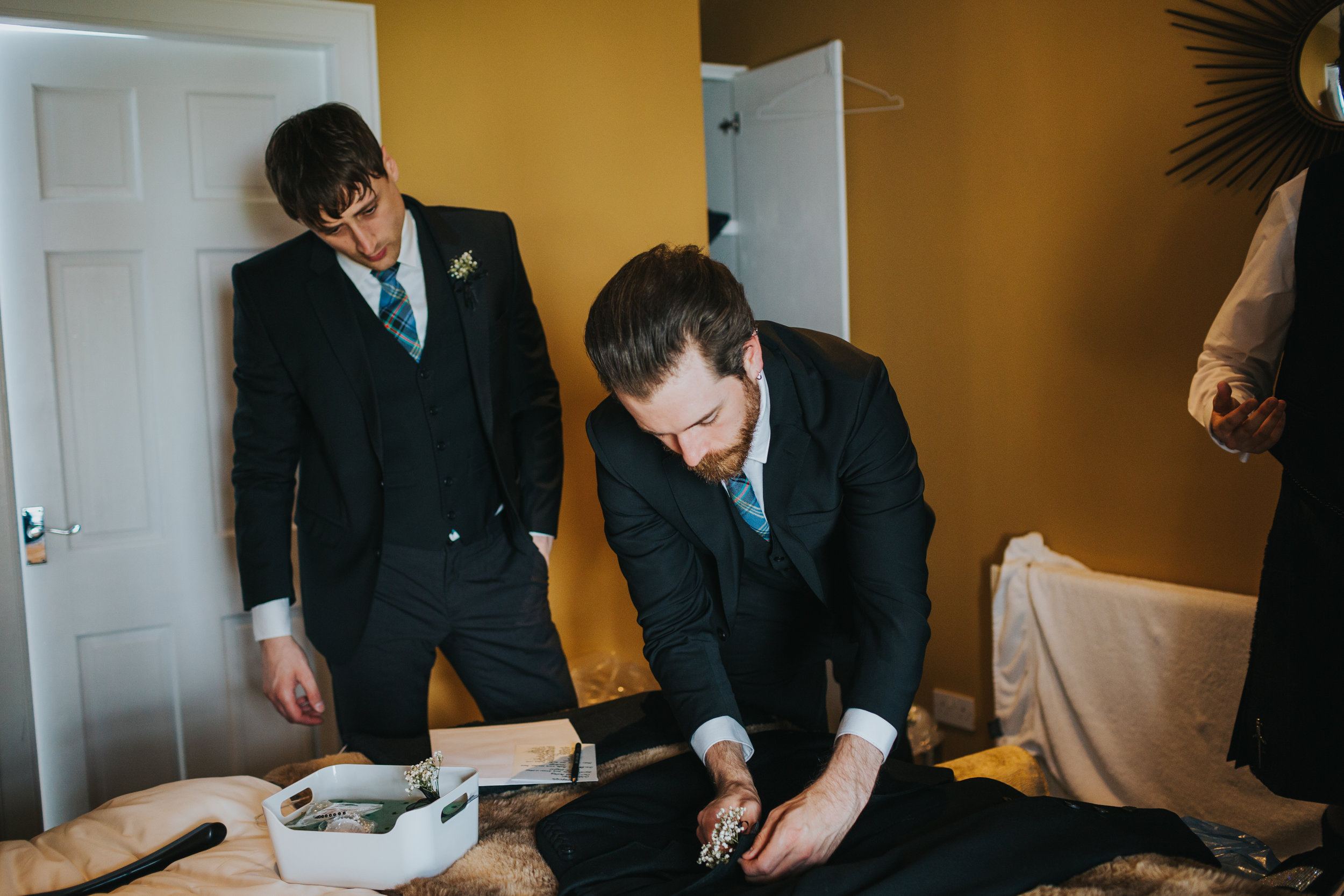 Groomsmen help prepare grooms suit. 