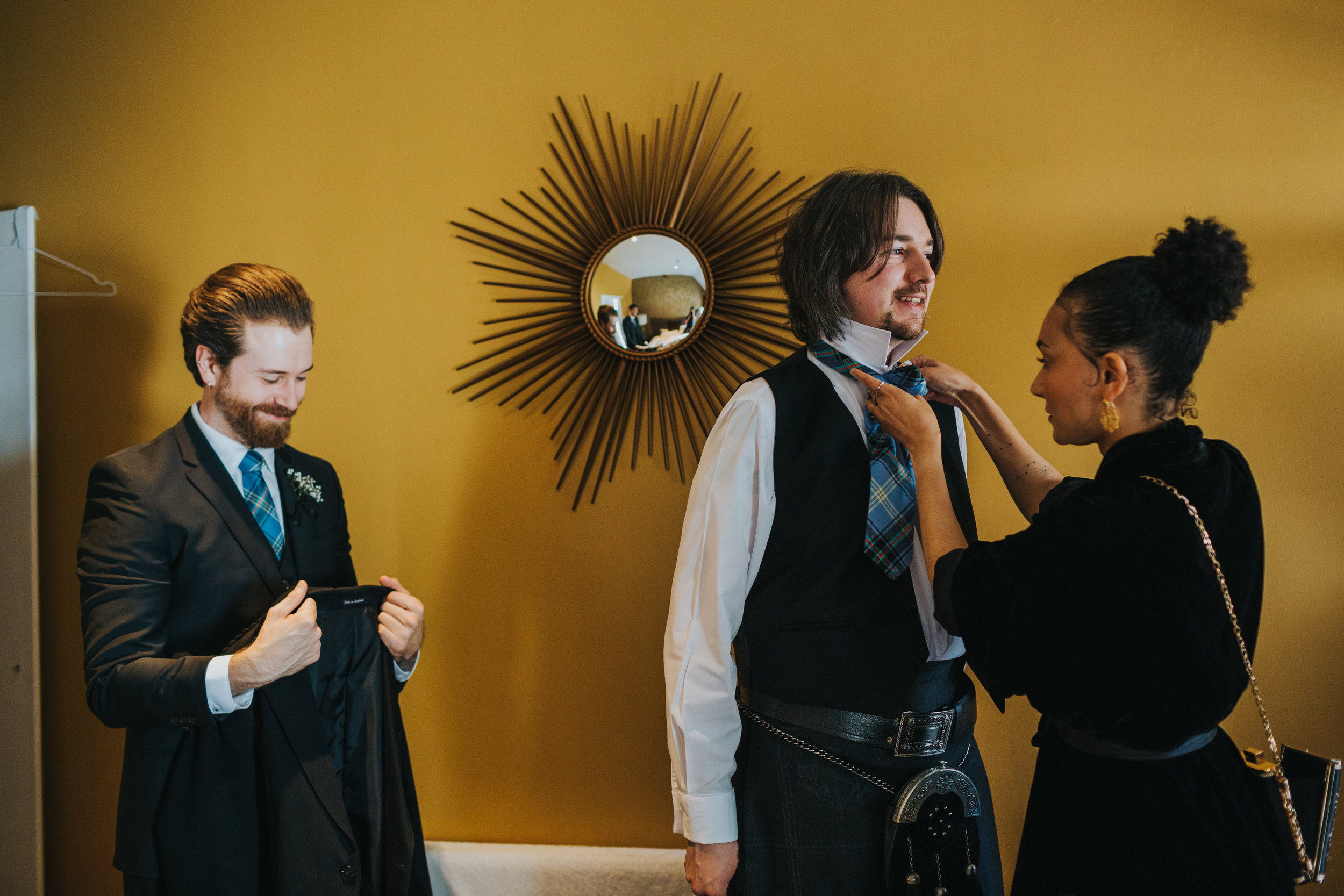 wedding guest helps Groom get dressed.