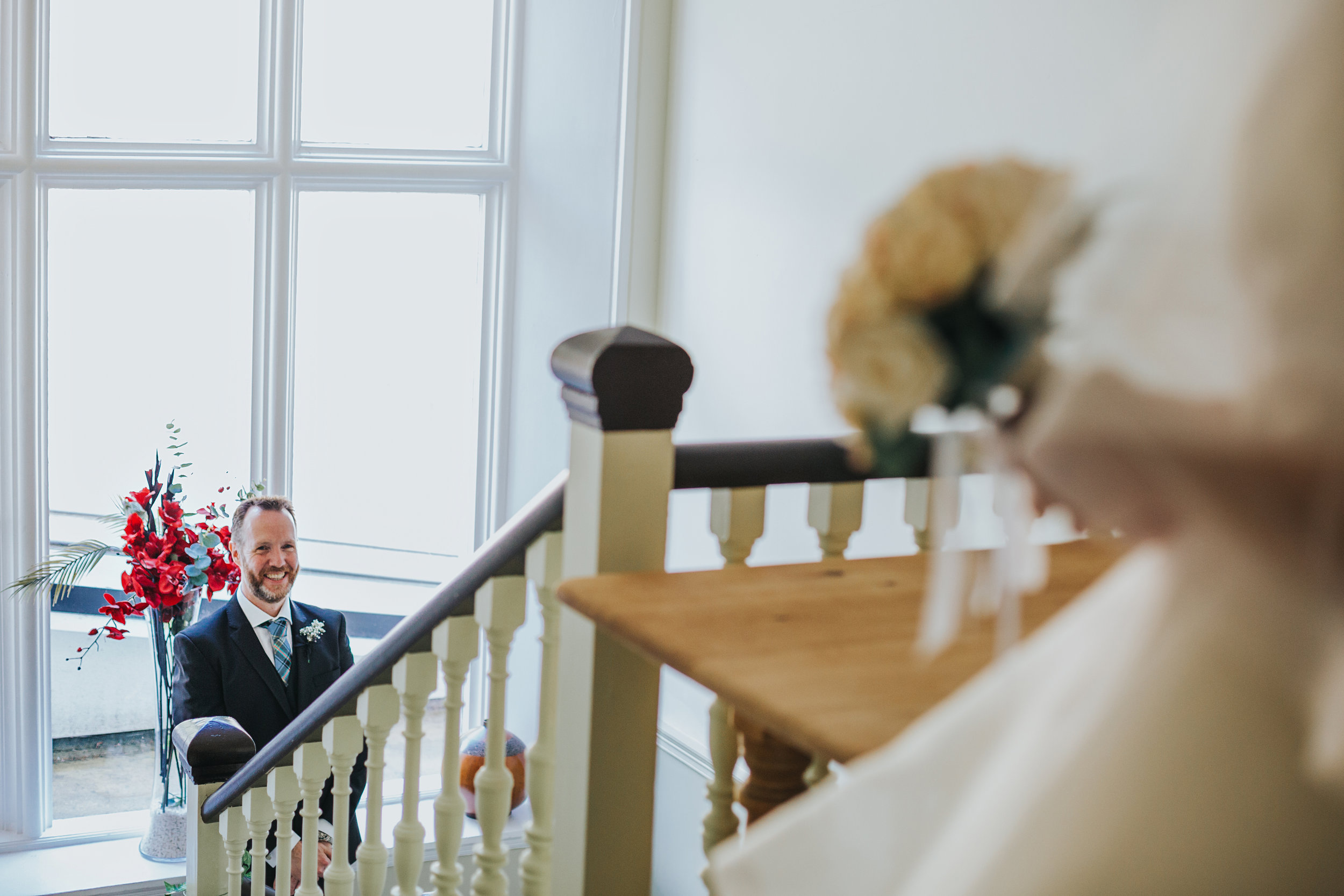 Brother of the bride is at the bottom of the stairs laughing at his sister.