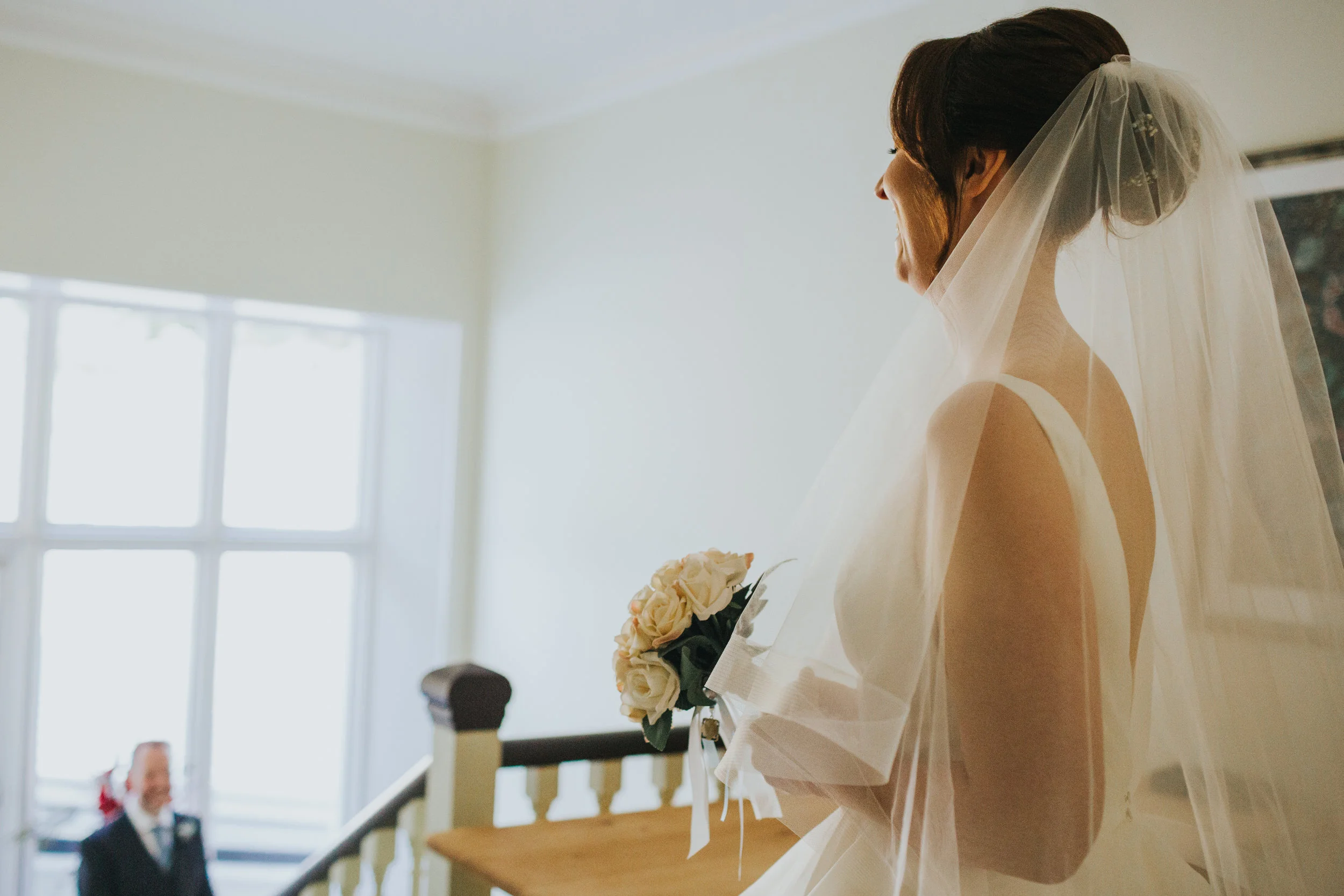 Bride stands at the top of the stairs smiling. 