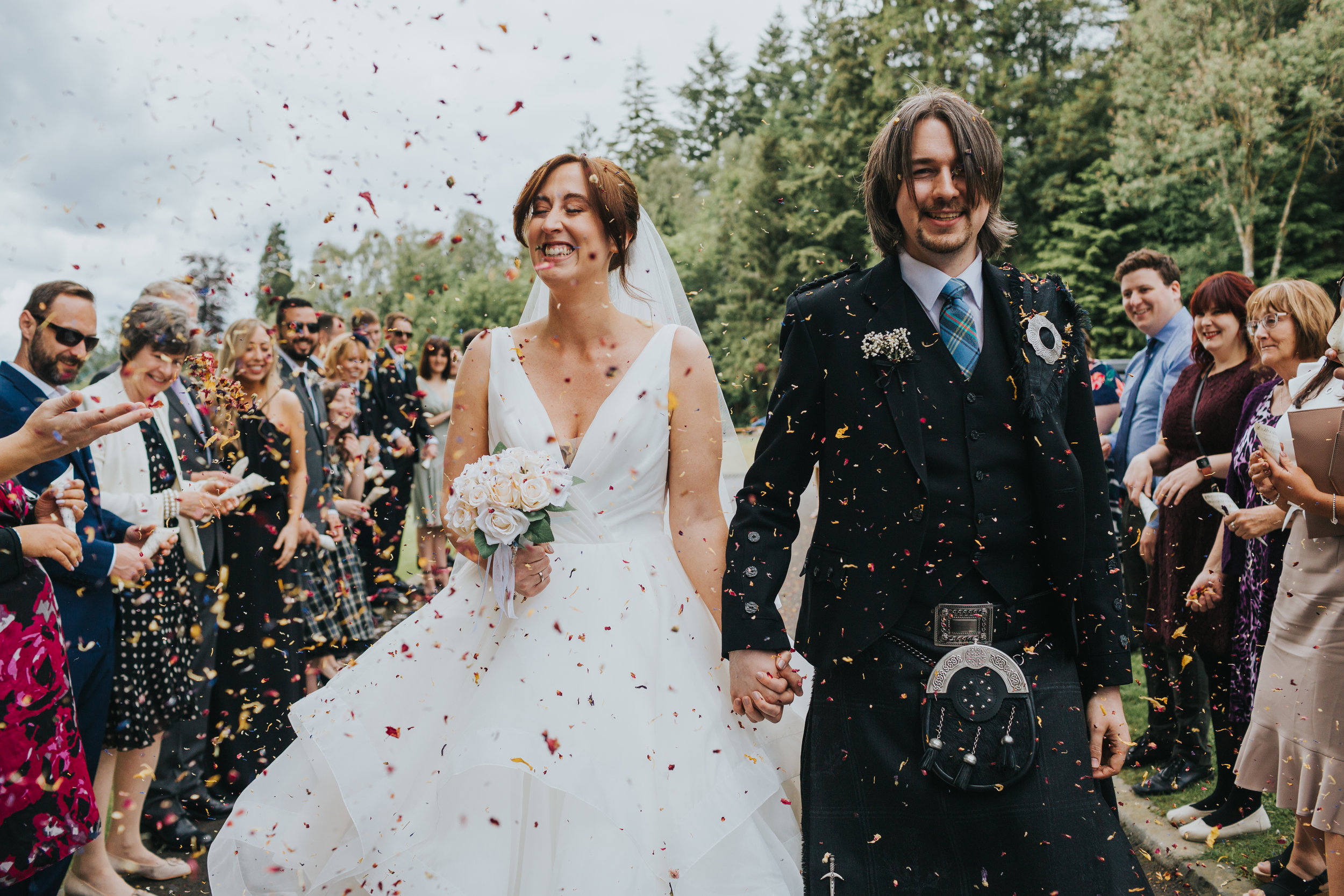 Couple laughing while confetti is thrown at them. 