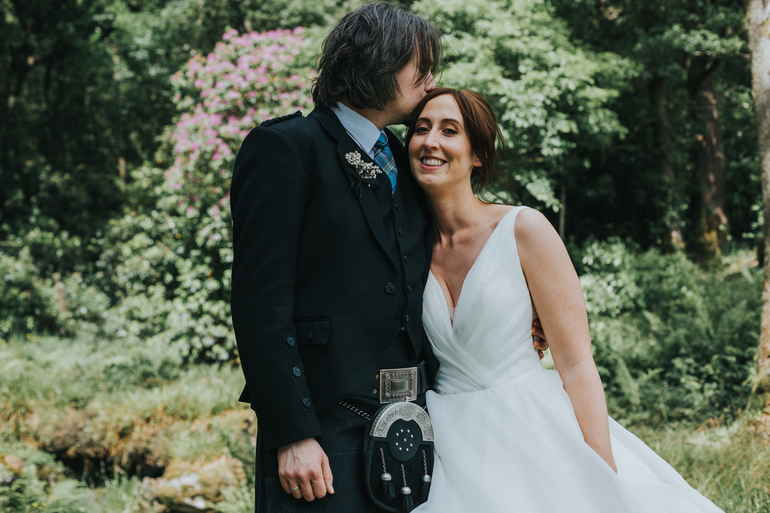 Bride and groom stand for photo near bushes in Scotland.