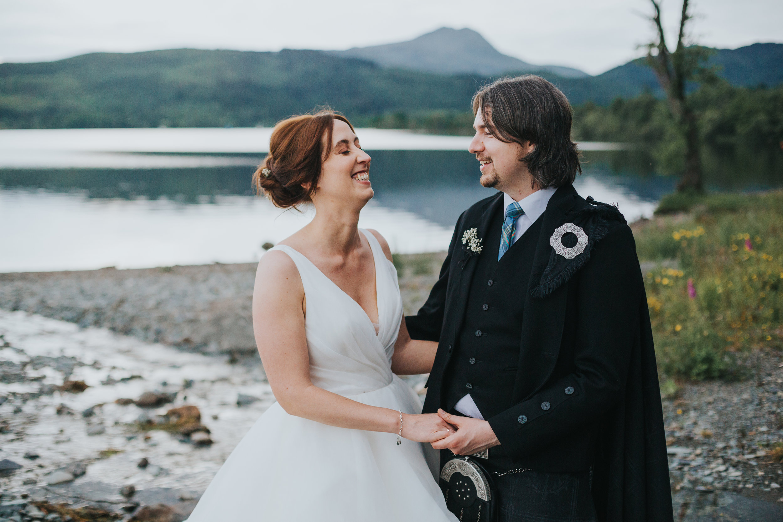 Bride and Groom laughing in front of Loch Ard. 