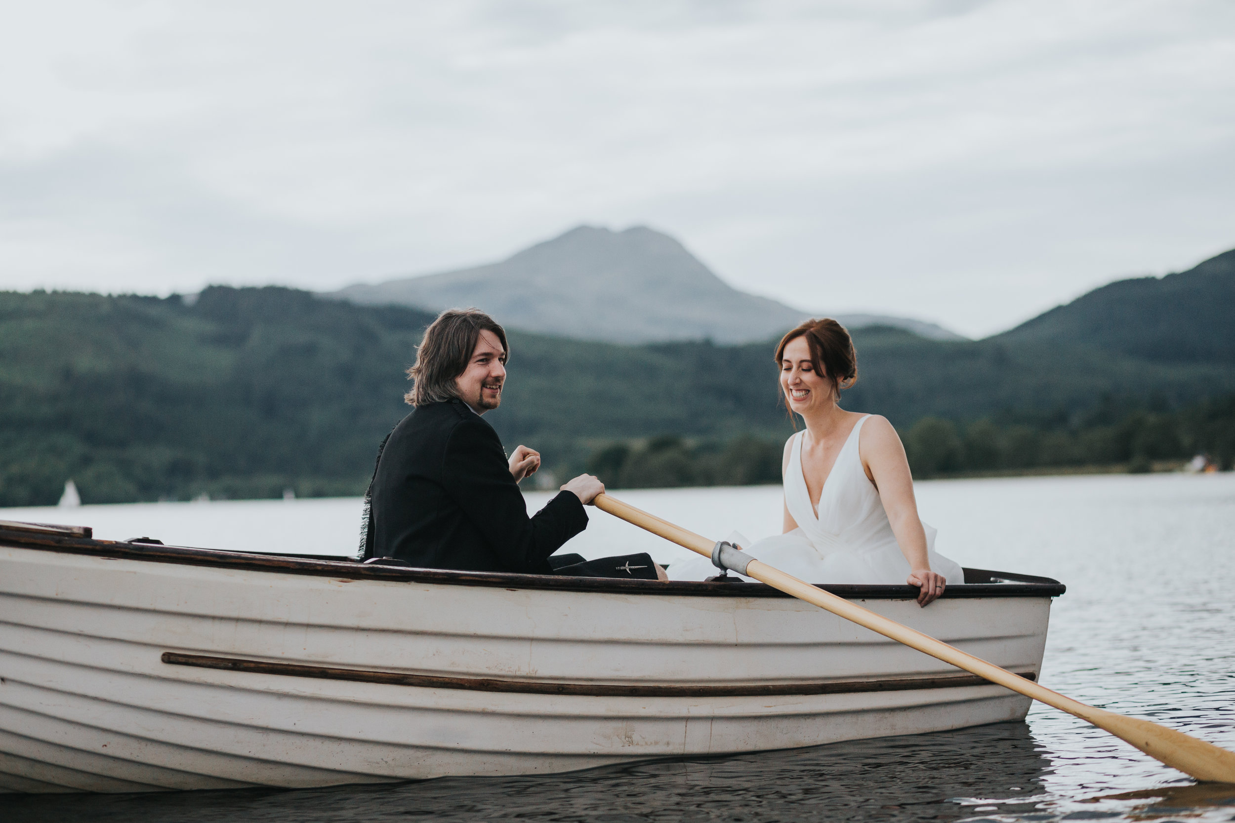 Bride and Groom laugh together in rowing boat on Loch Ard on their Wedding day.