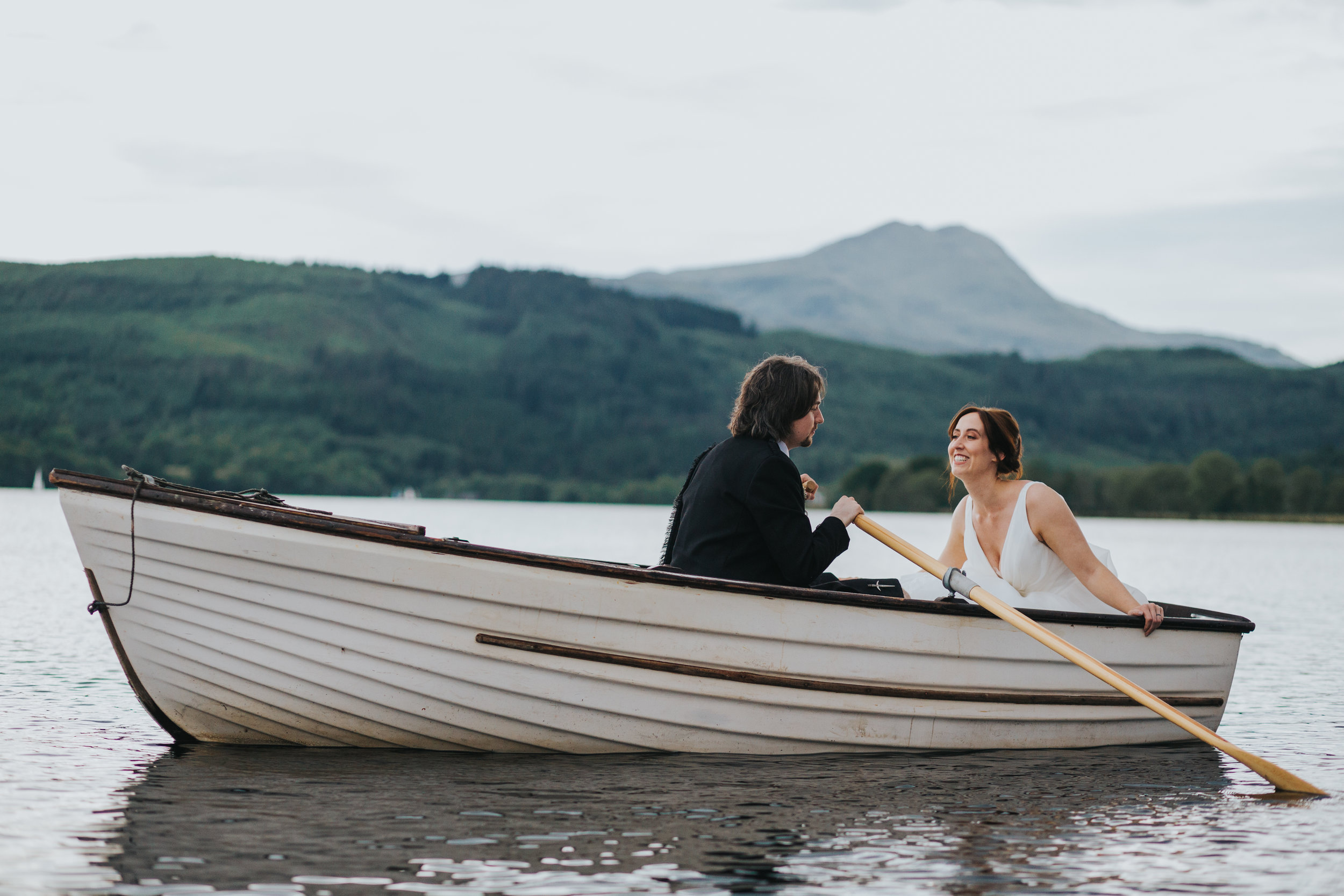 Bride leans towards her groom as her rows them across Loch Ard on their wedding day. 