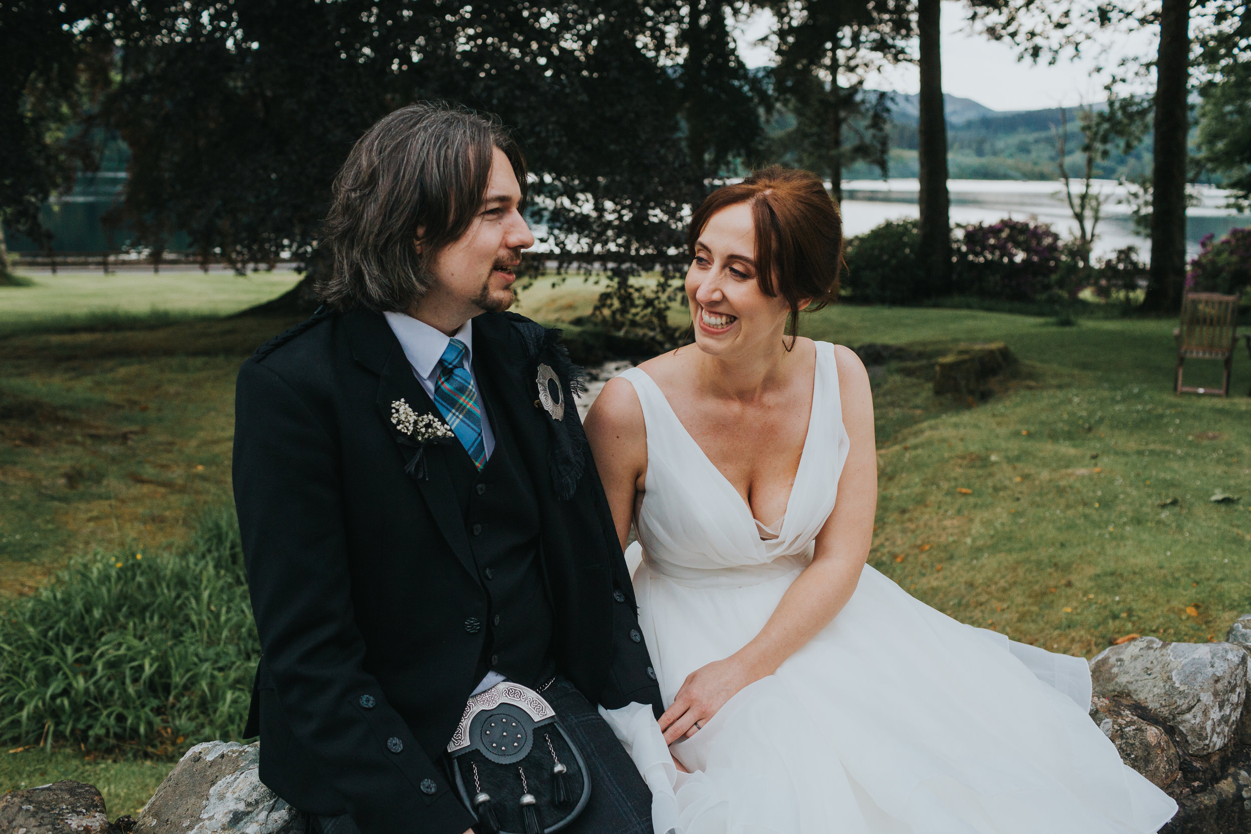 Bride laughing at groom while sitting on wall. 