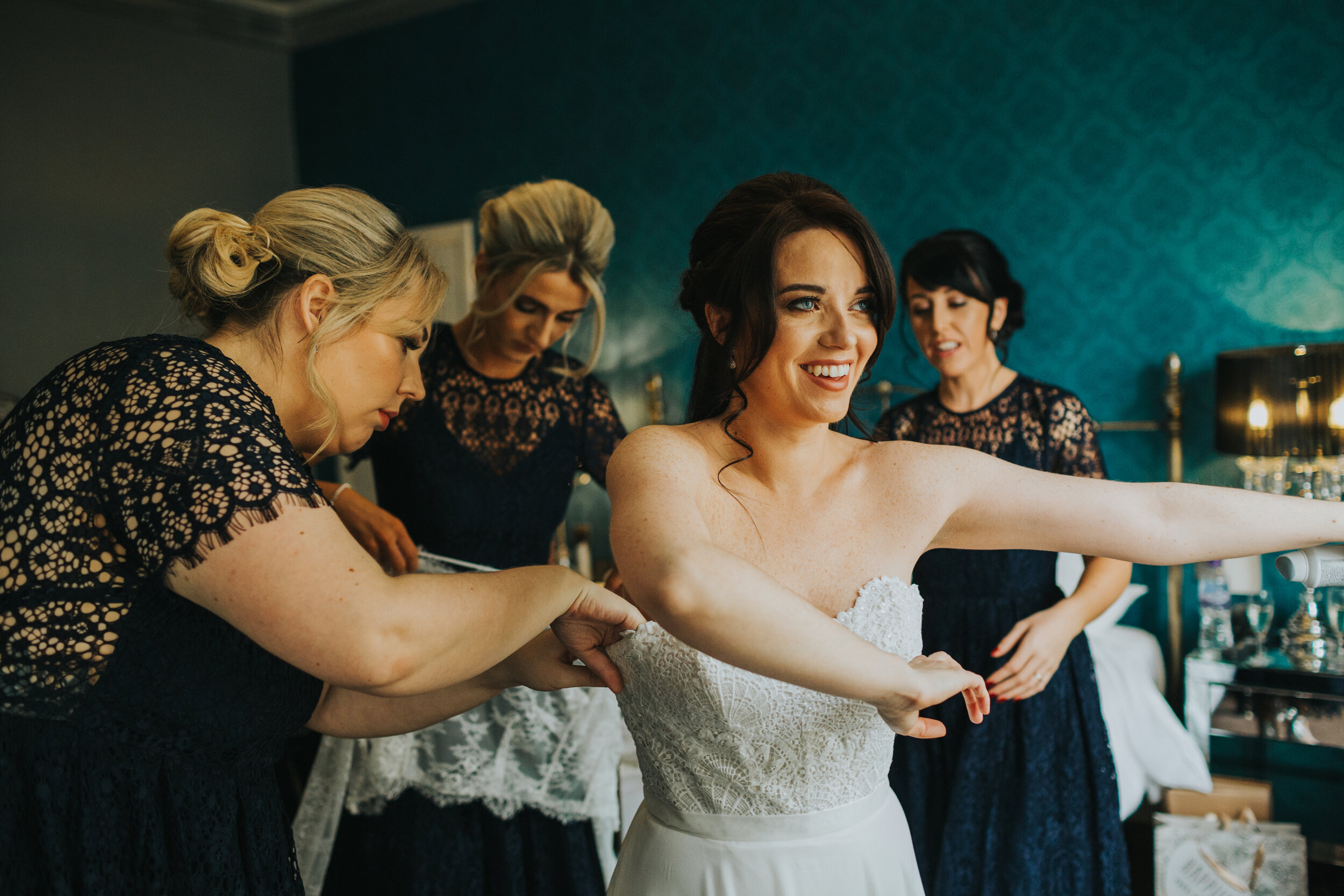 Bride smiles as she is helped into her wedding dress. 