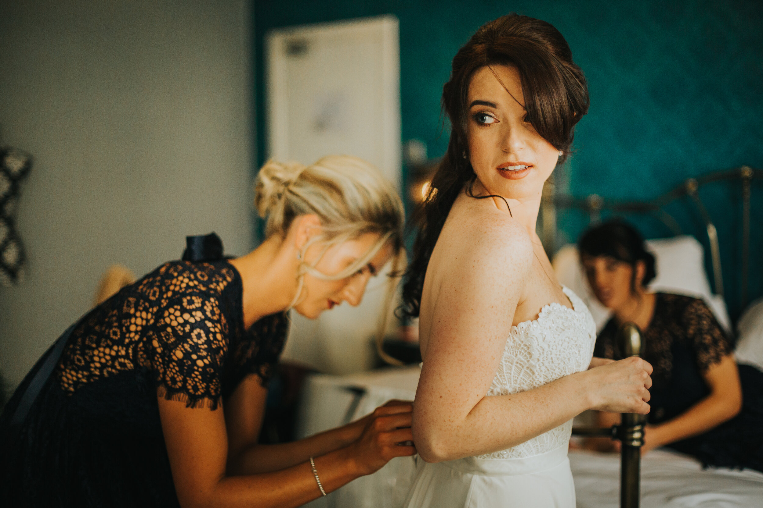 Bride looks at herself in the mirror as the finishing touches are done to her wedding outfit. 