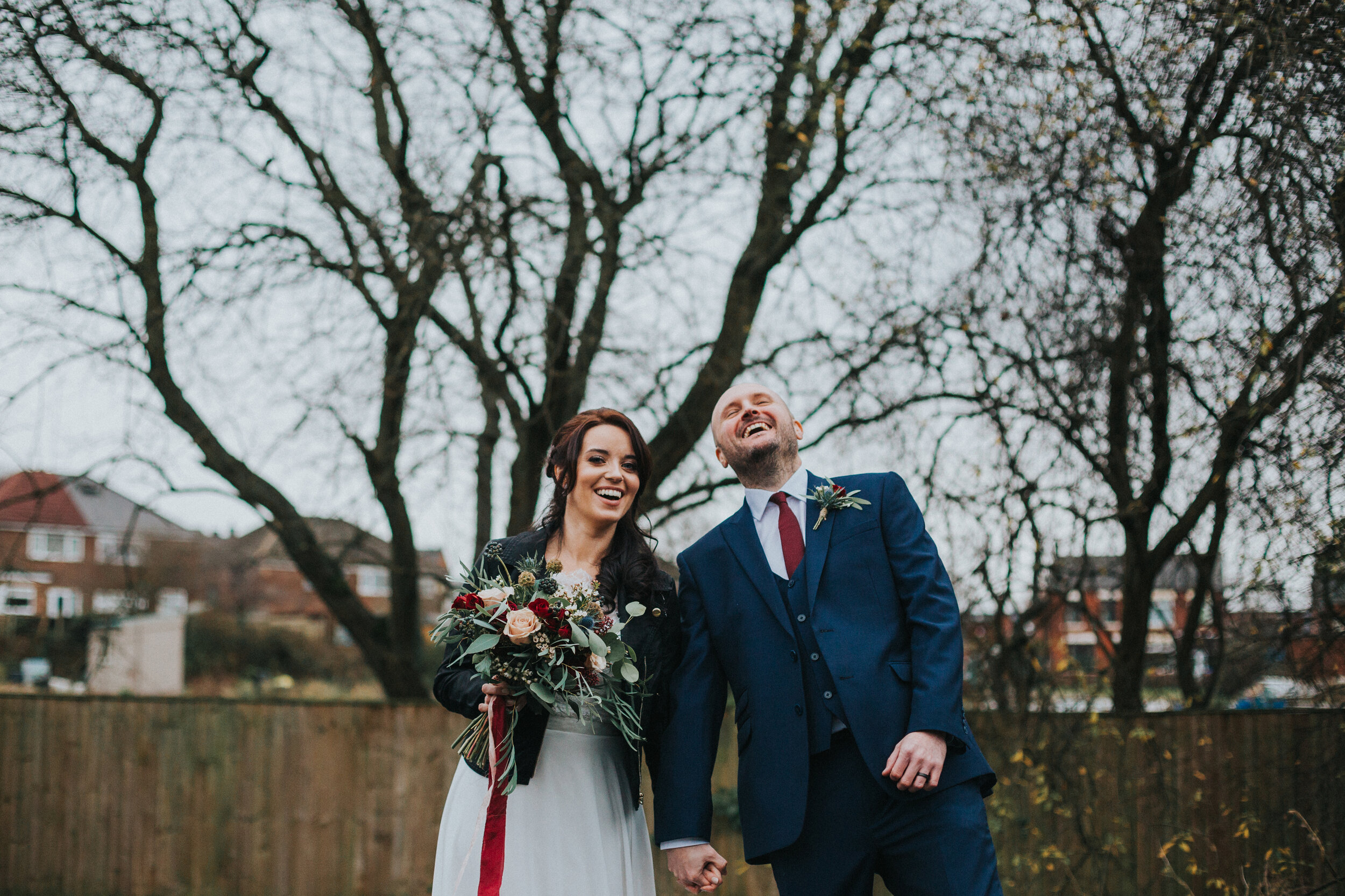 Bride and Groom laughing with trees behind them on a winters day.