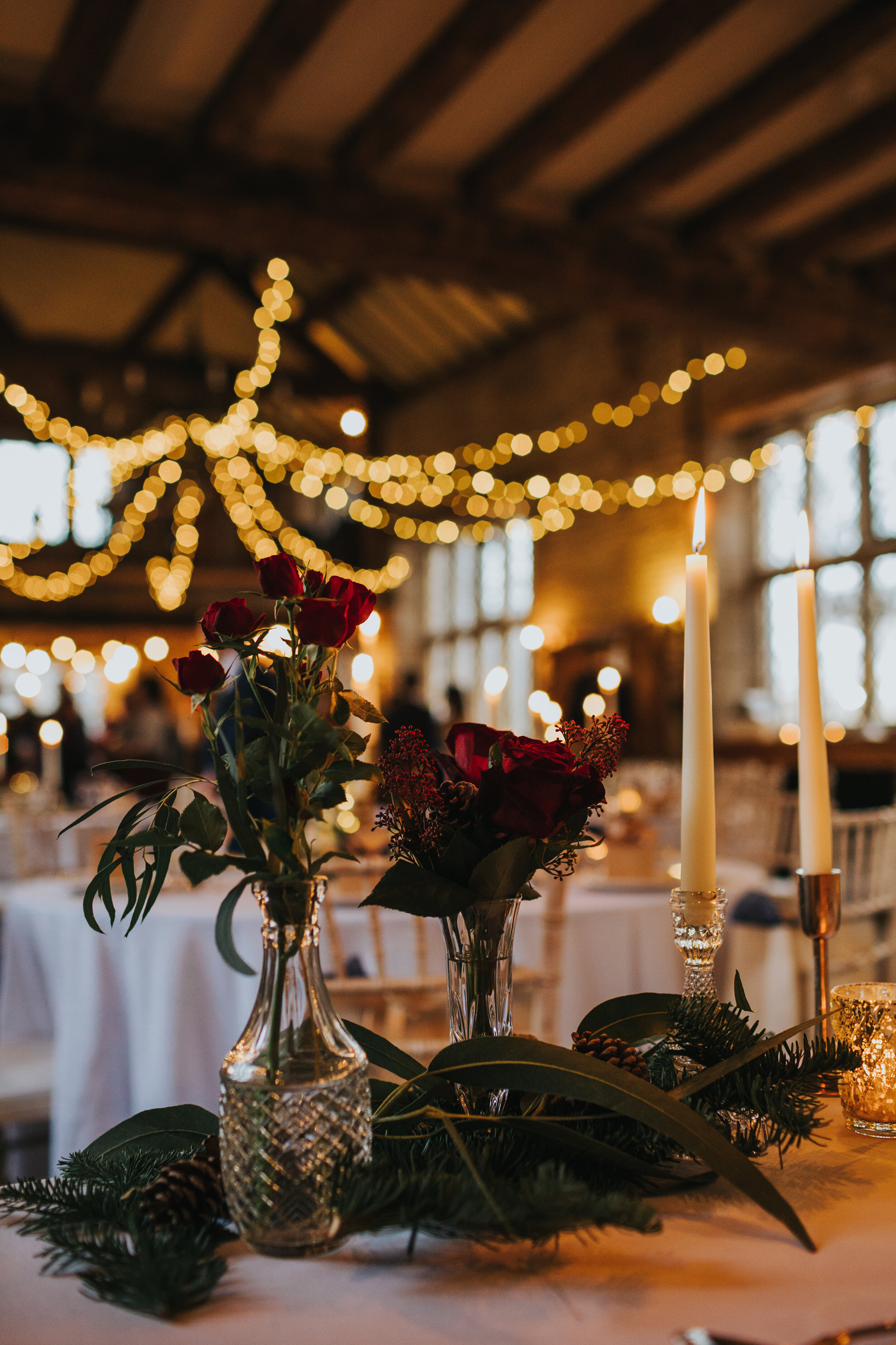 Red roses and evergreen foliage as a table decoration with fairy lights behind. 