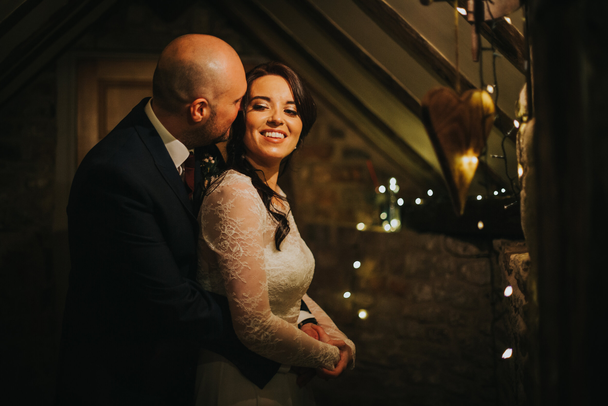 Bride and groom have a cuddle in The Old Grammar School next to some fairy lights. 