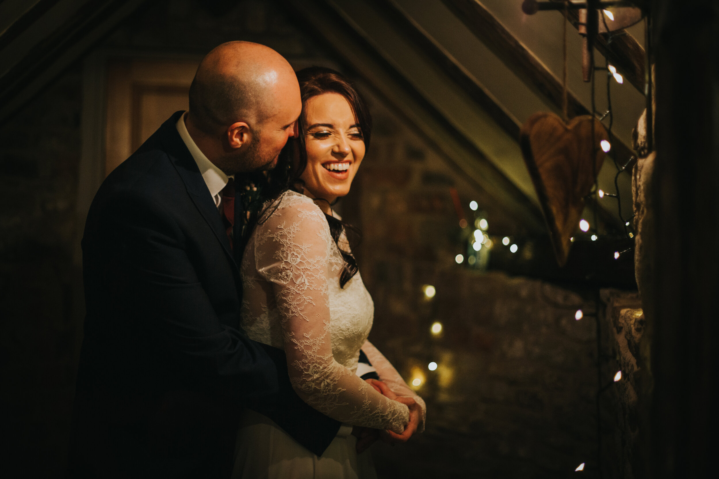 Indoor portrait of bride and groom at their winter wedding in Manchester as they share a cuddle and a laugh. 