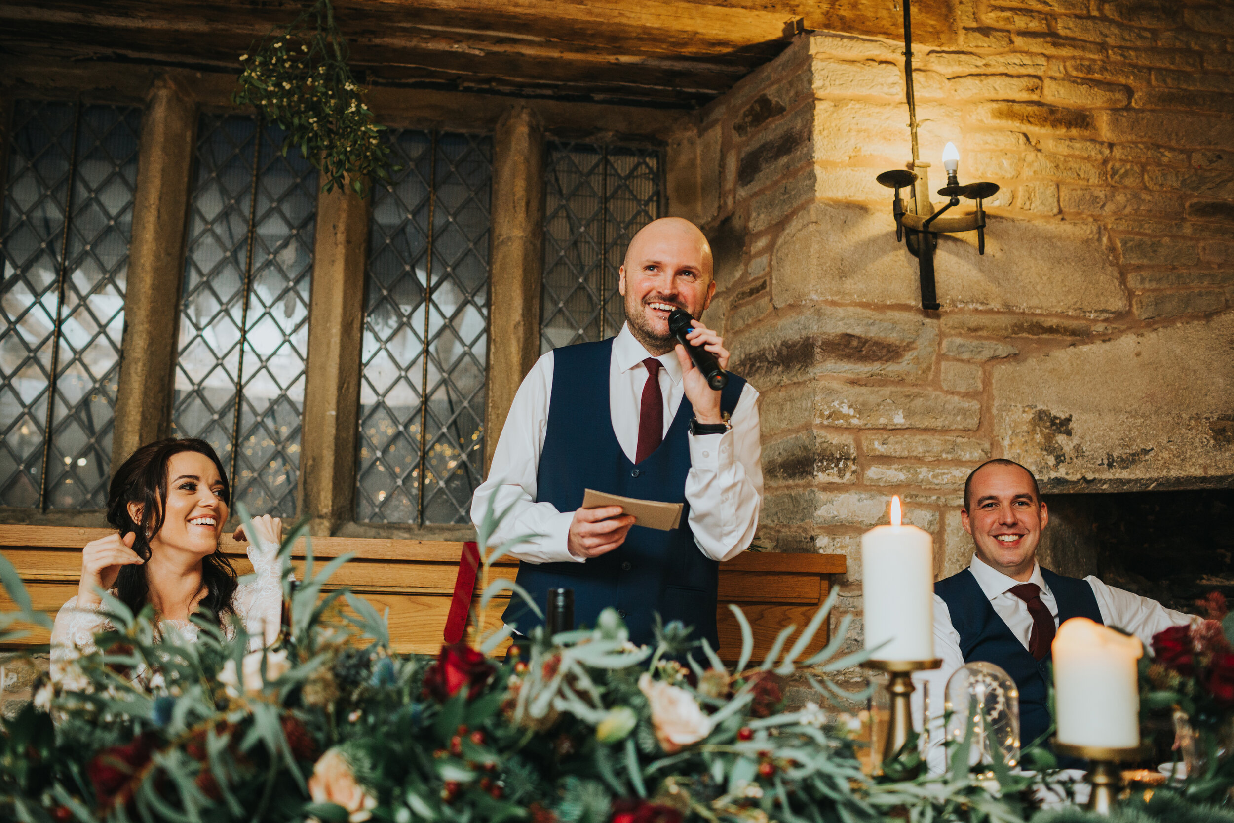 Groom laughs making his speech while standing  under mistletoe. 