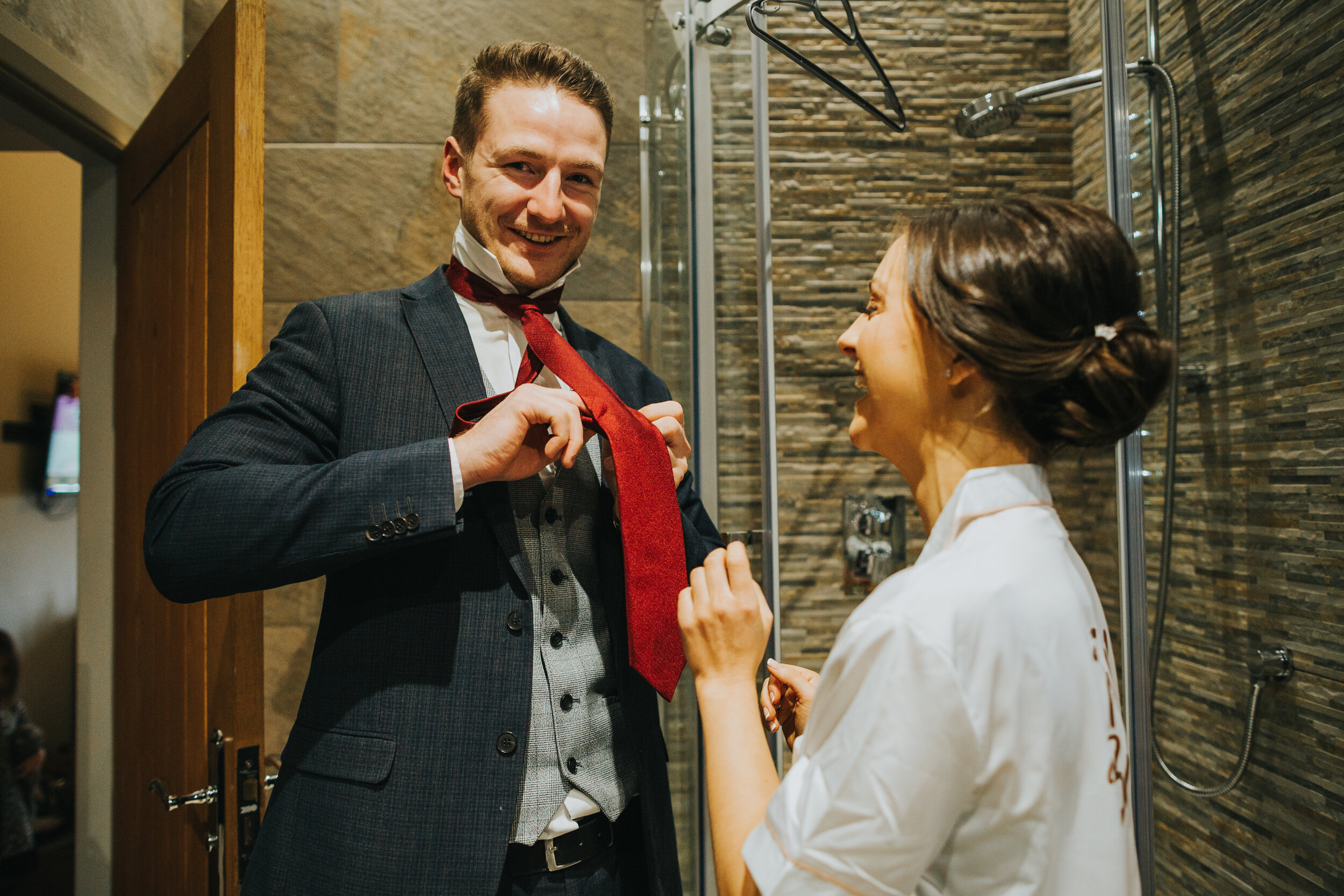 Groomsman gets his red tie put on in bath room at White Hart Inn