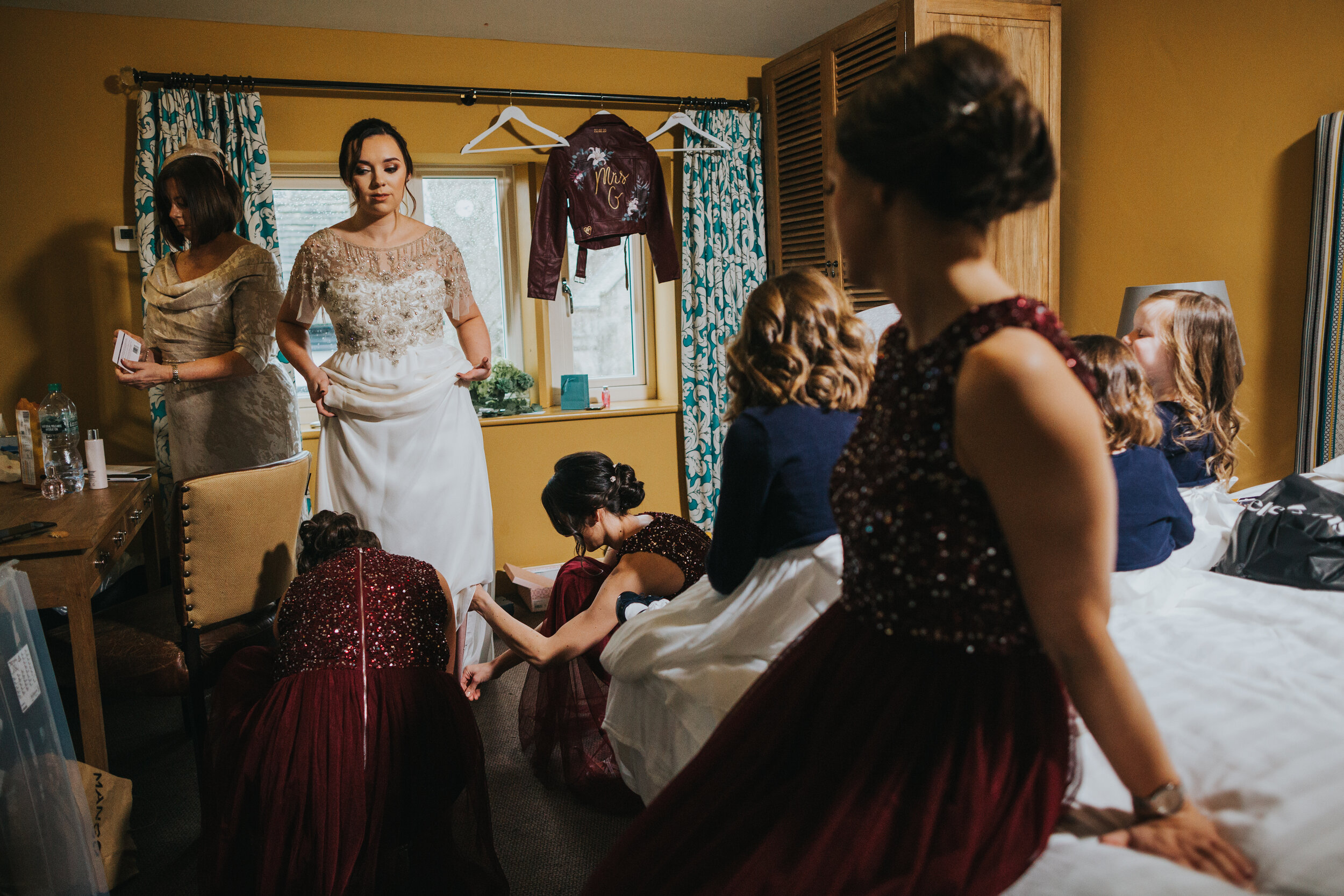 Bride is surrounded by her friends wearing her wedding dress. 