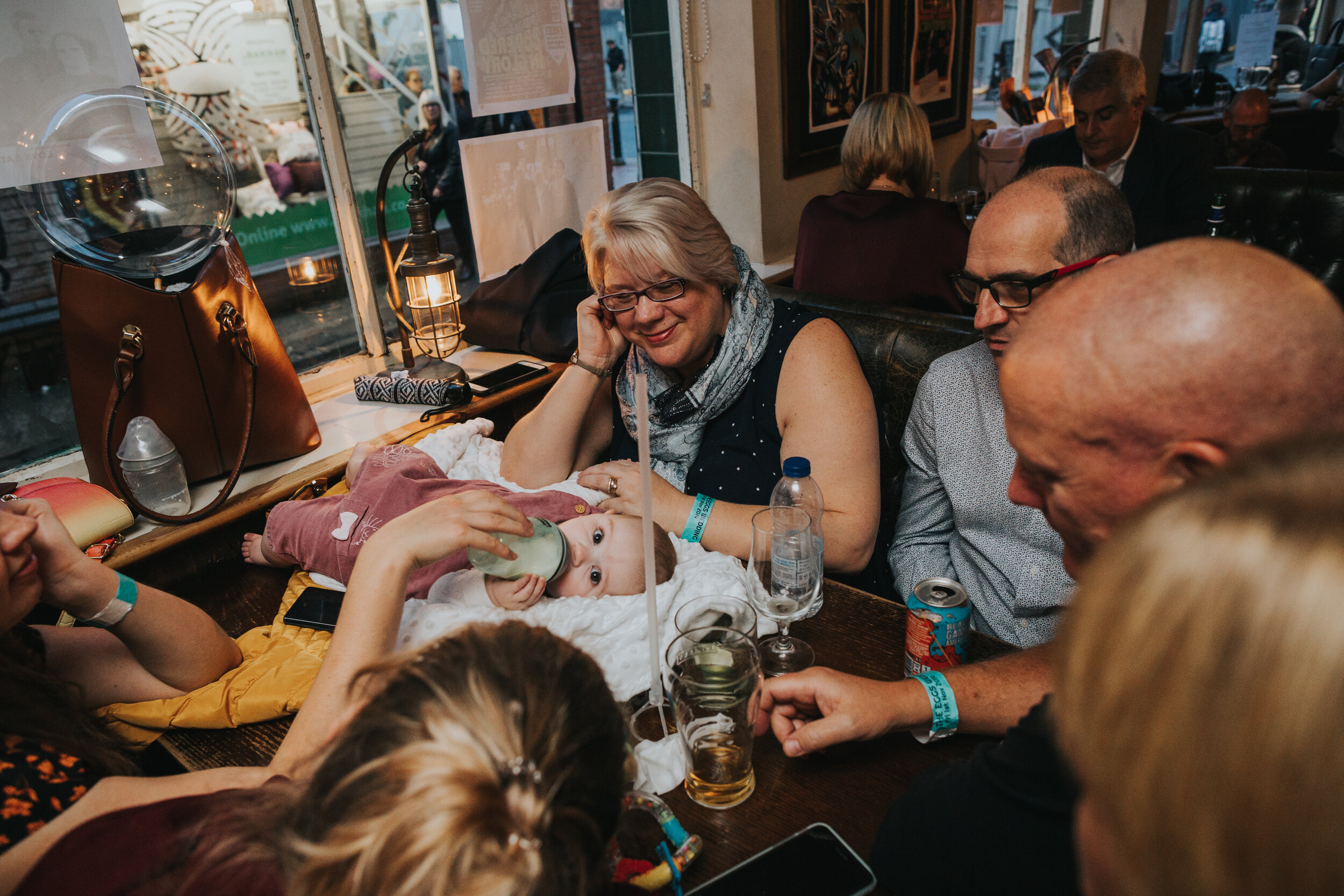 Baby drinks bottle lying on pub table surrounded by wedding guests.  (Copy)