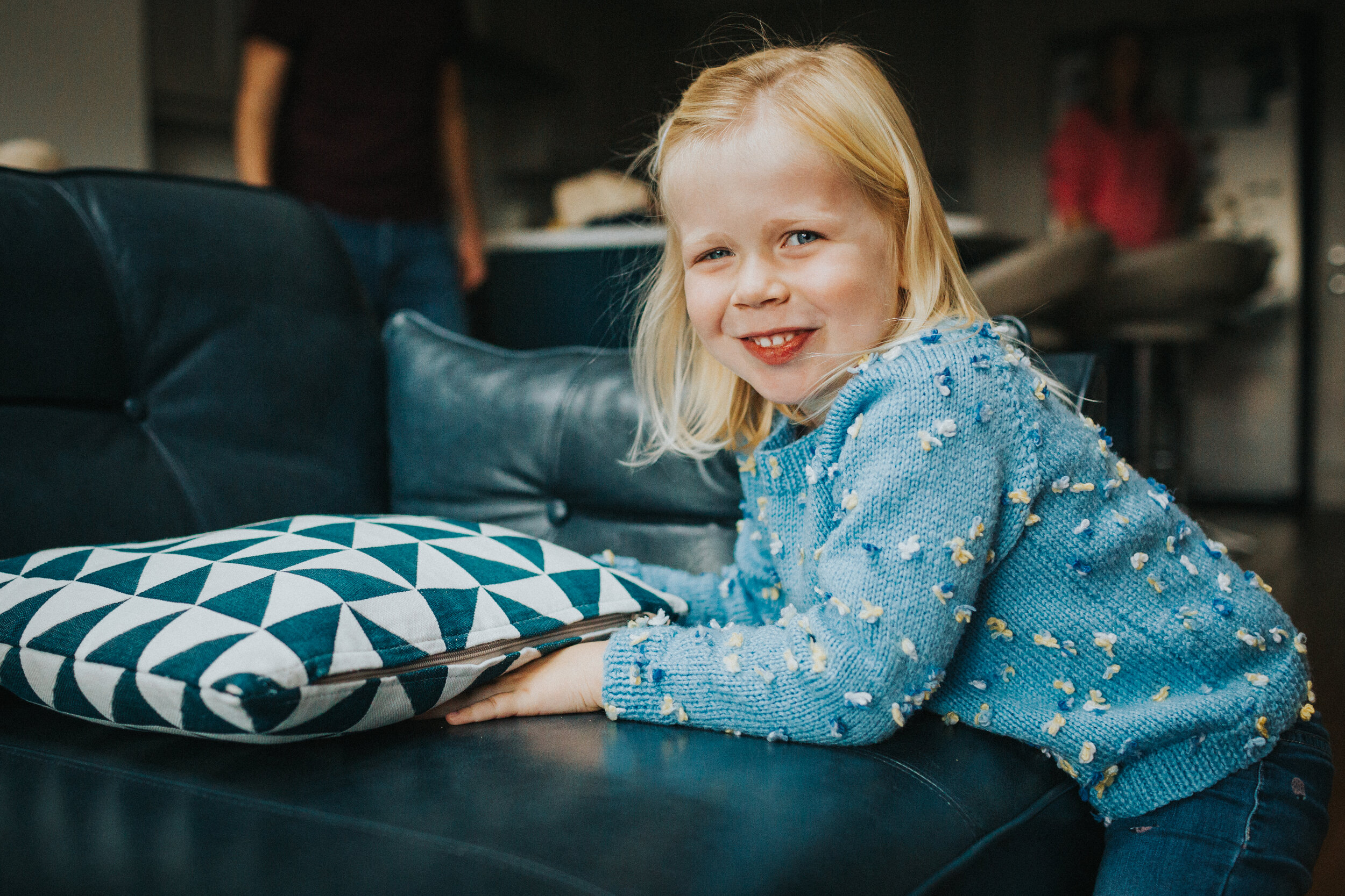 Little girl leans on sofa in family home and smiles for a photo.