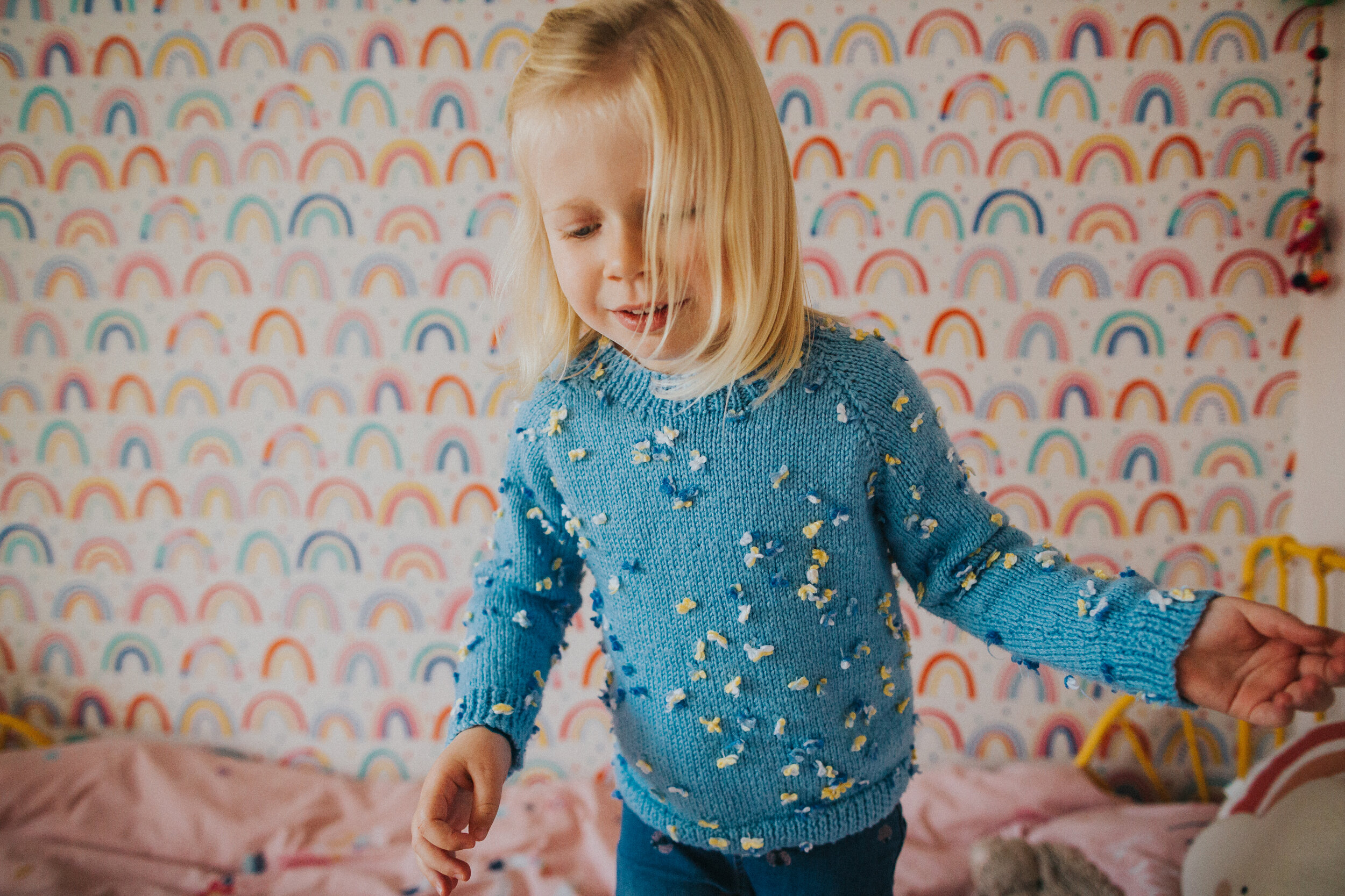 Little girl stands in front of her rainbow wall paper.