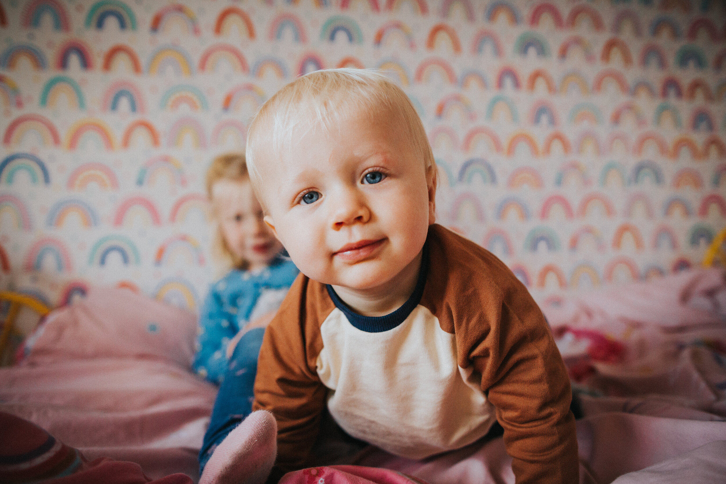 Little boy crawls up to camera with rainbow wall paper behind him. 