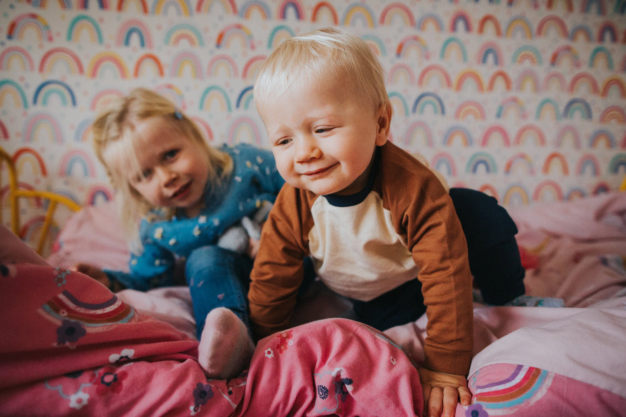 Little boy has a cheeky grin as he climbs off the bed. 