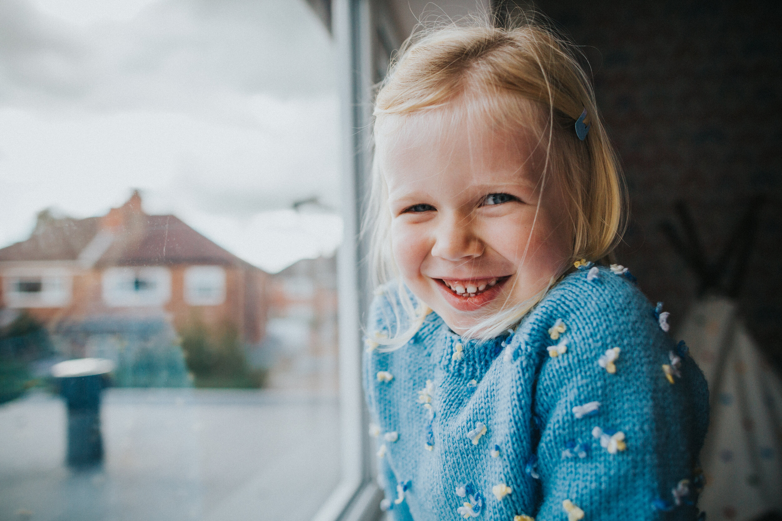 Little girl smiles for a photo next to her bedroom window. 