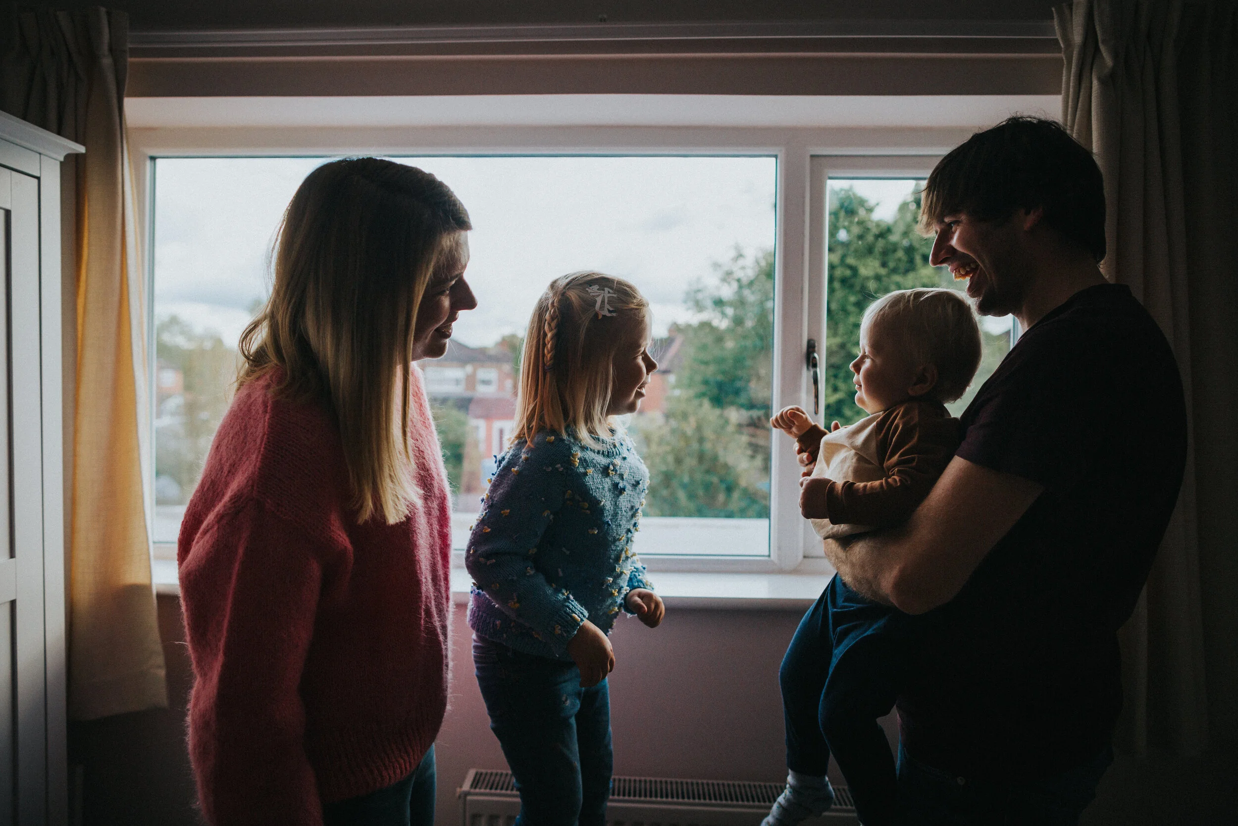 Little girl and boy play with each other as their parents hold them. 