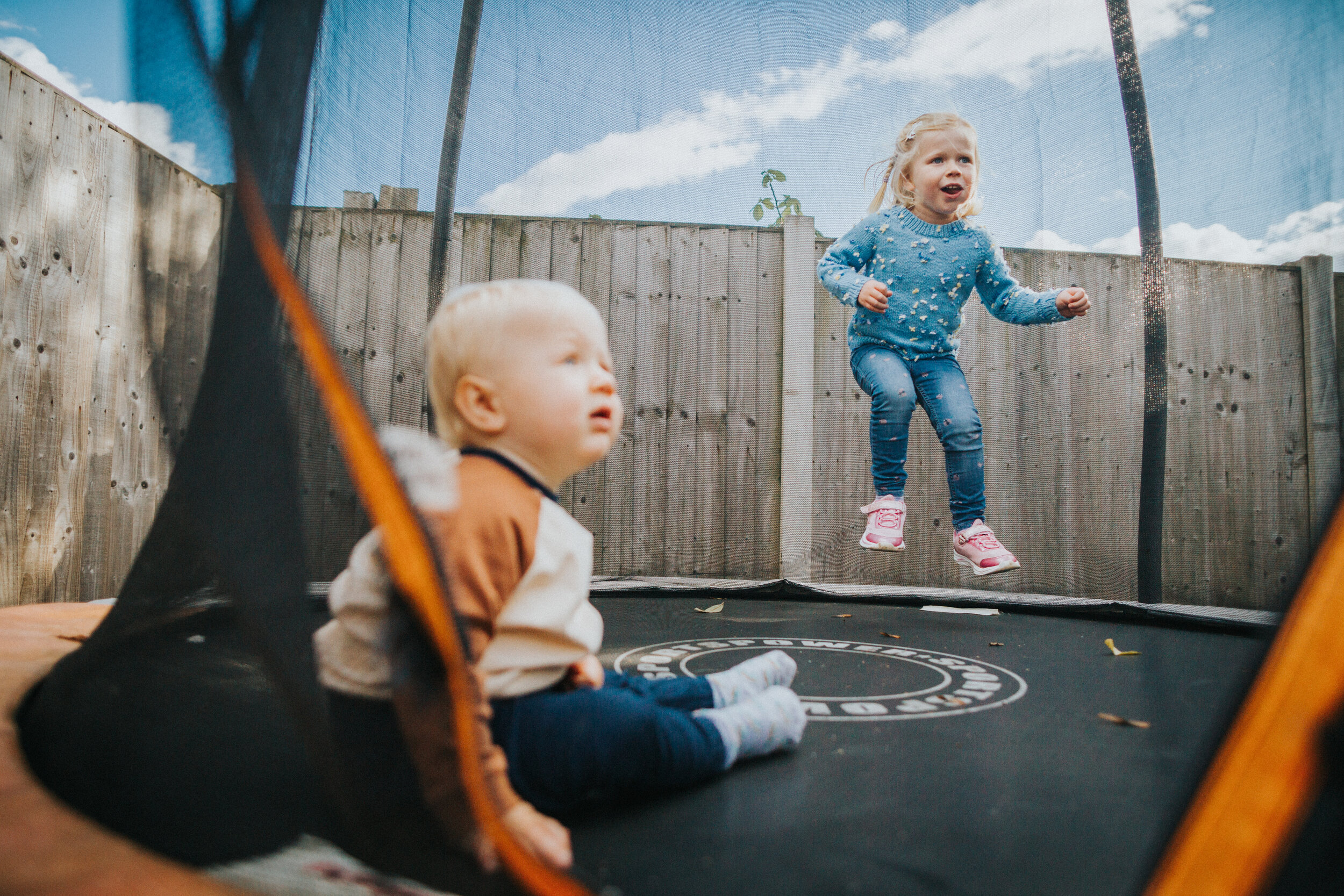 Little girl jumps on trampoline with her baby brother. 