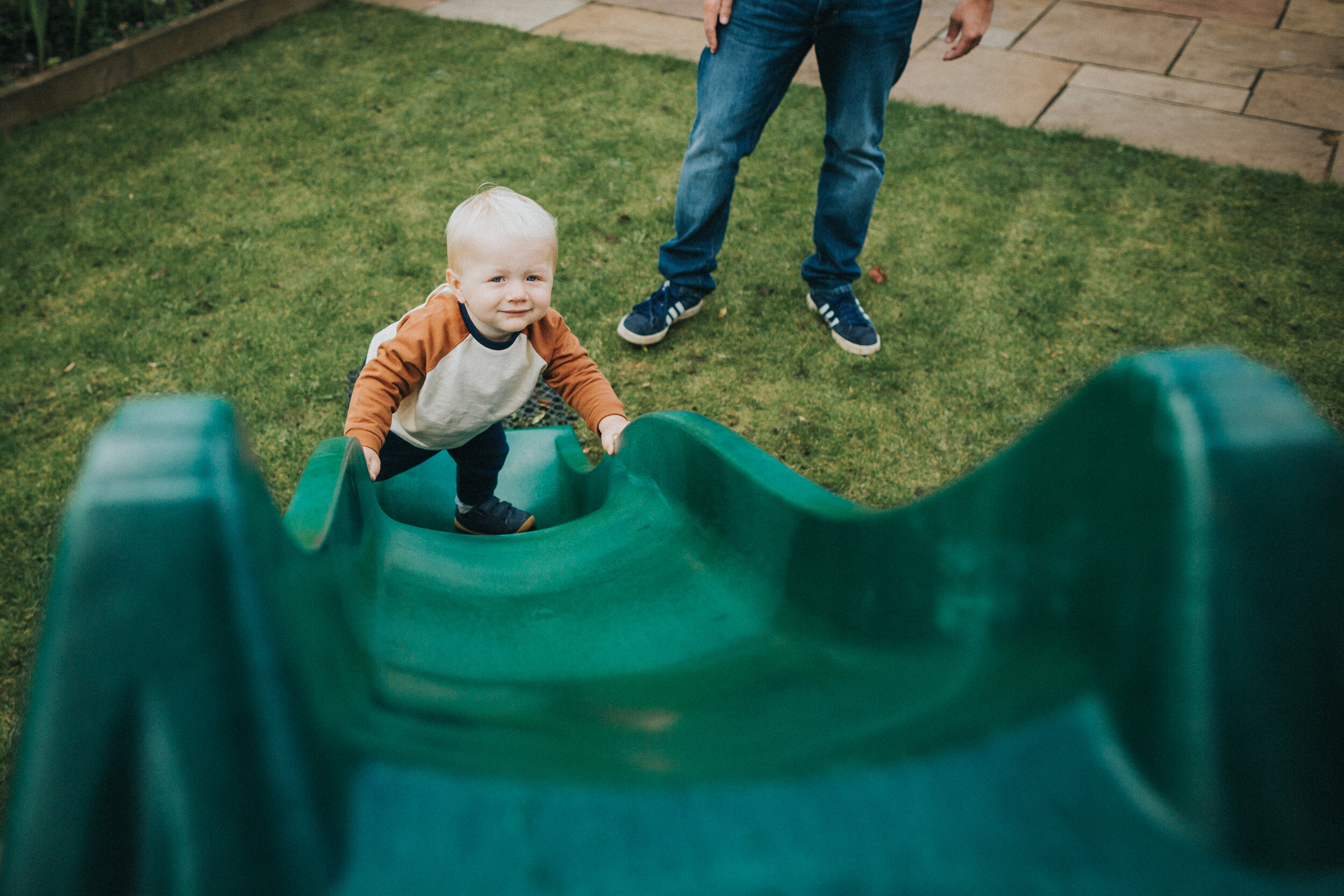 Little boy climbs up green slide. 