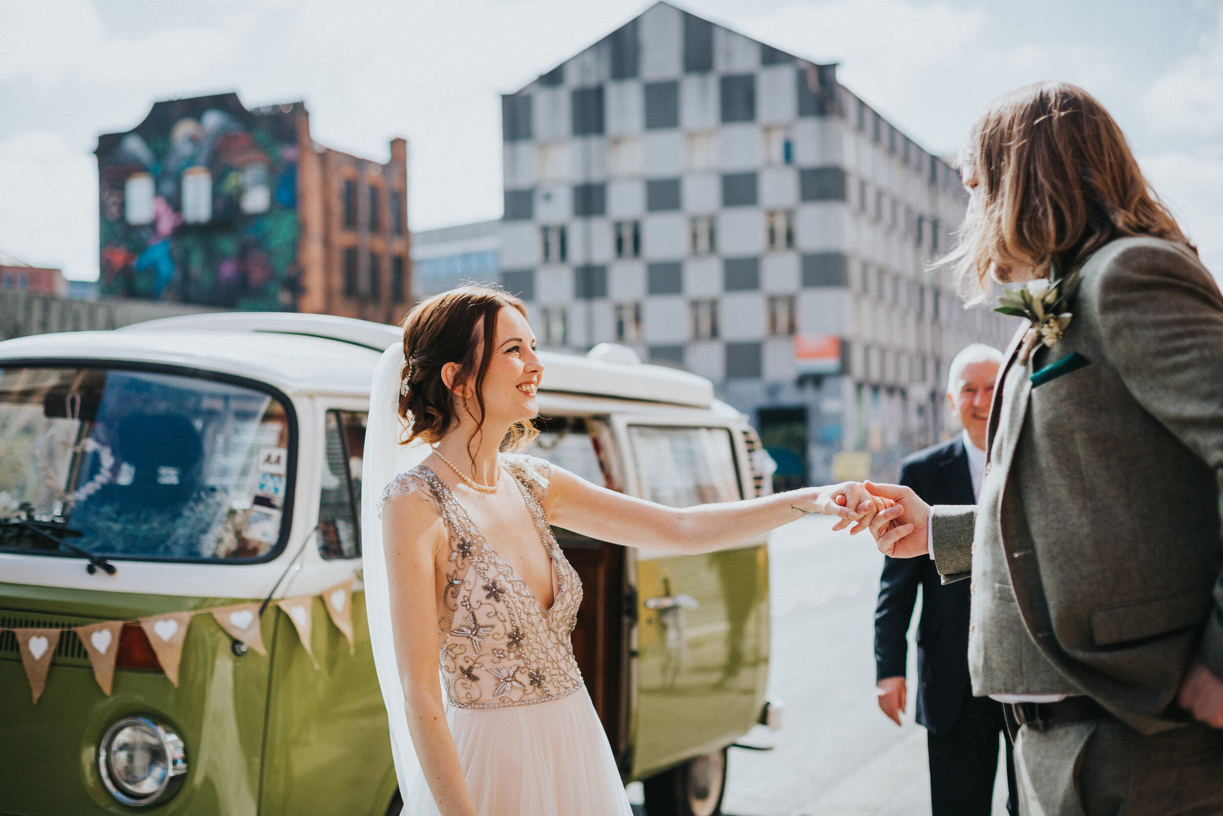 Bride and Groom hold hands next to green VW camper van and take each other in before going off to get married. 