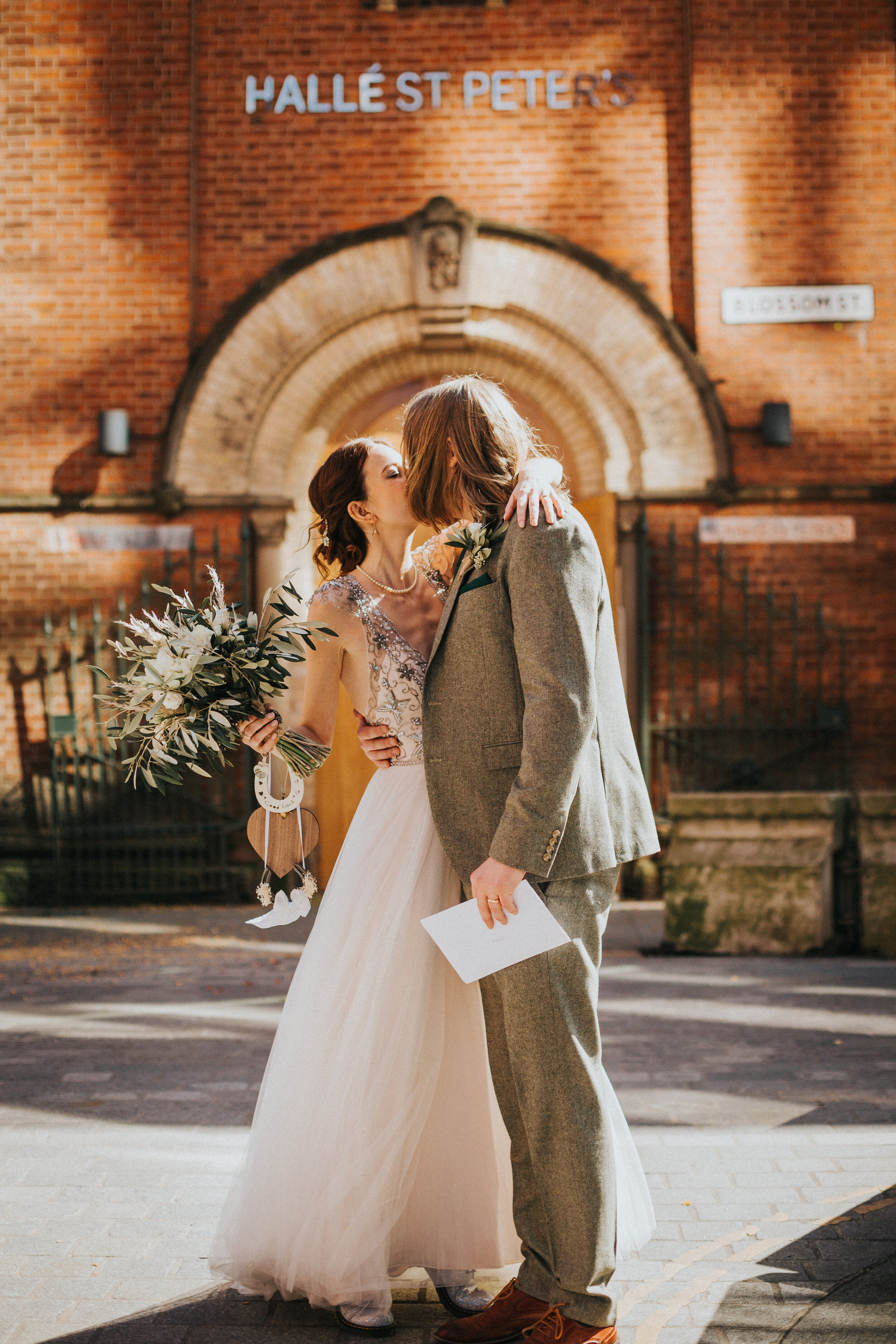 Bride and Groom kiss outside Halle, St Peter's, Manchester in the sunshine on their wedding day. 
