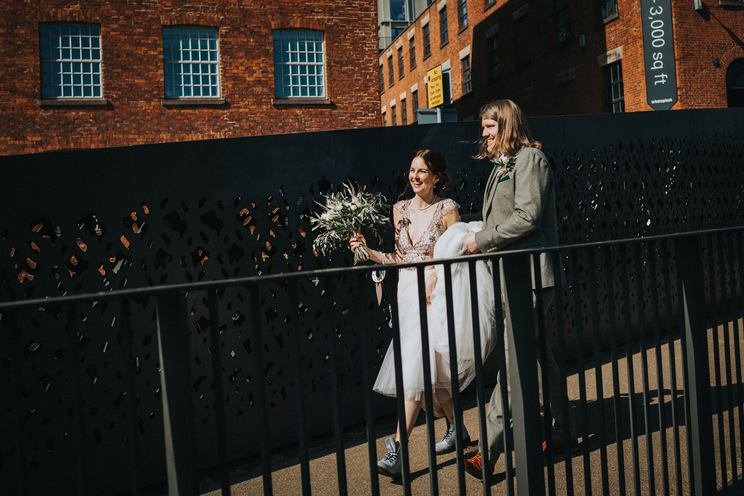 Bride and groom walk together laughing as they approach the canal in Manchester City Centre. 