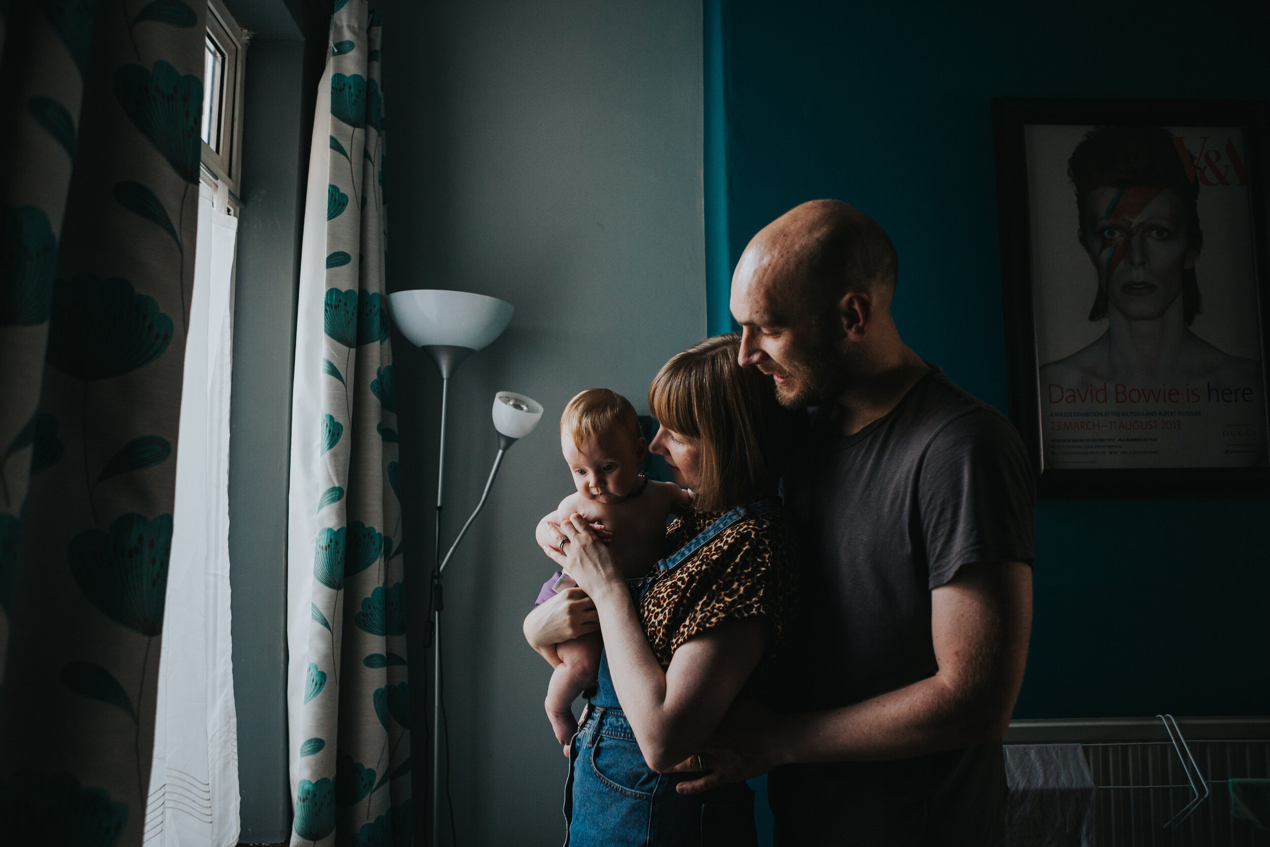 Family stand for a photo by the window with David Bowie print behind them. 