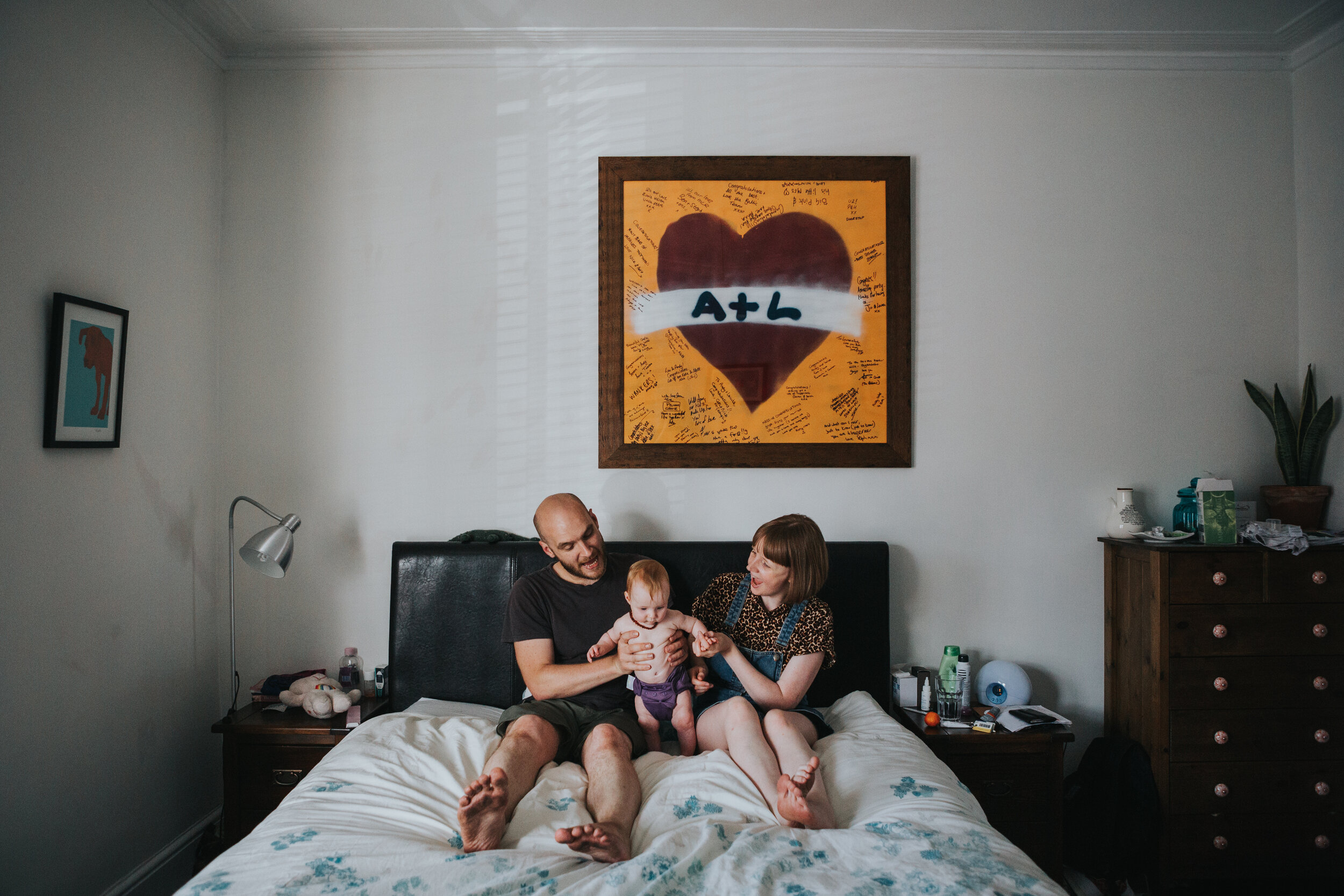 Mum and dad play with their baby on the bed at their home in Chorlton, Manchester. 