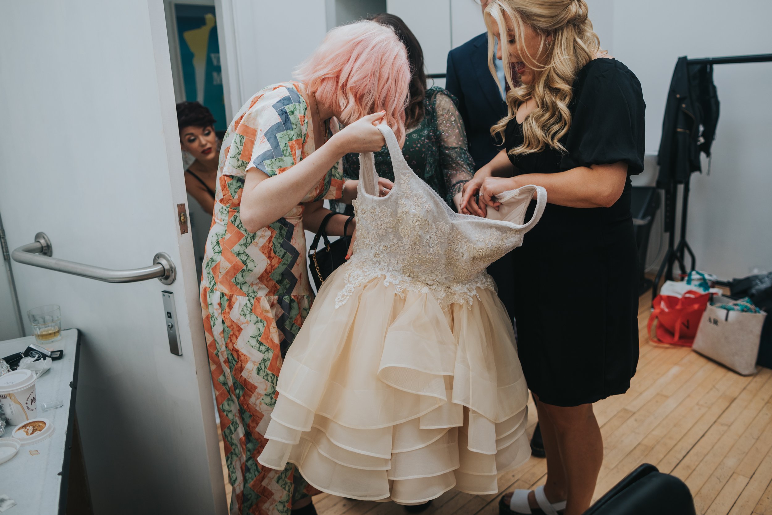 Bridemaids prepare wedding dress as the Bride peeps out from the loo. 