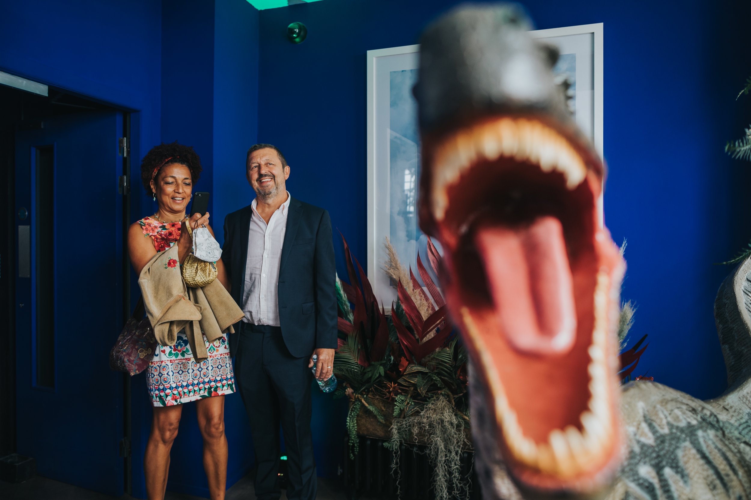 Wedding guests look on behind the toothy mouth on a Velociraptor. 