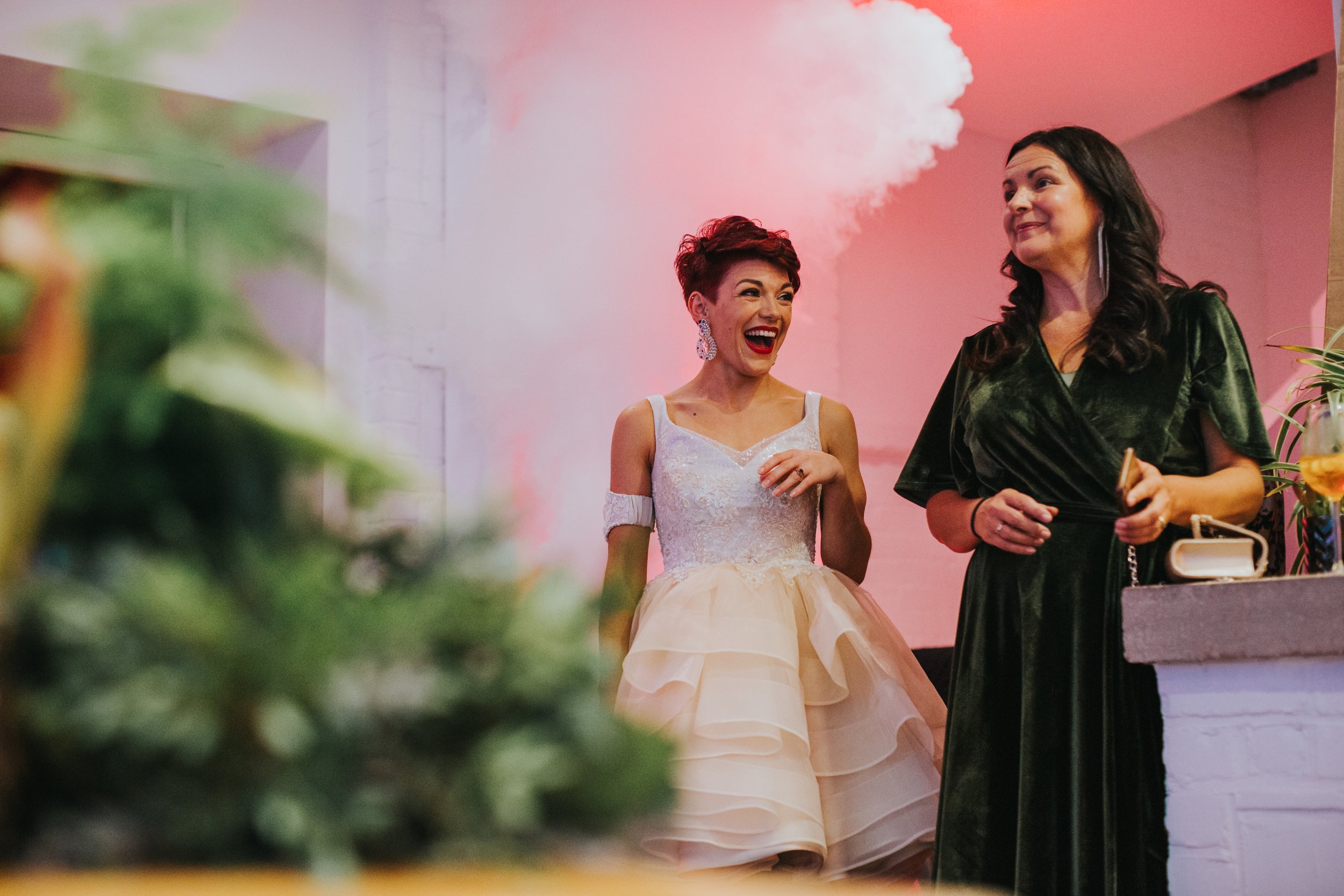 Bride and her mother laugh as the dry ice fires behind them. 