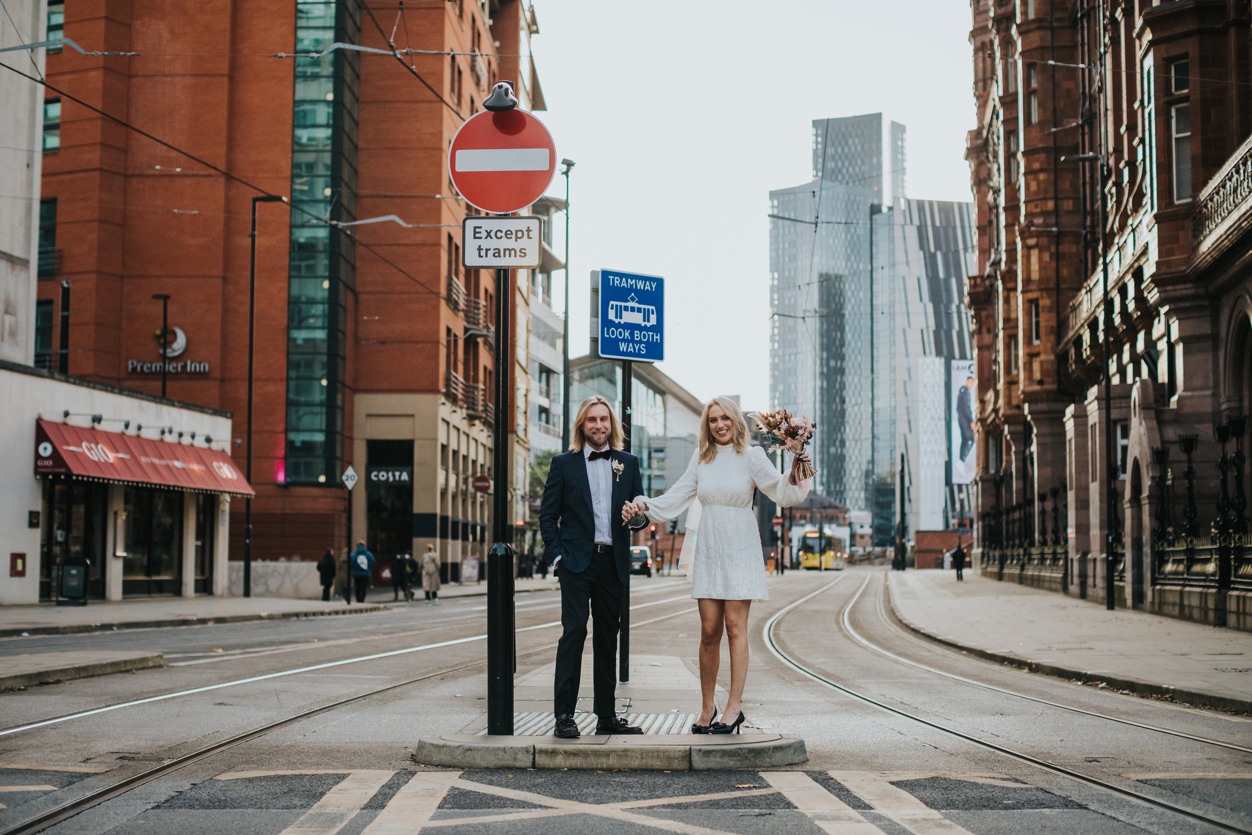 Bride and groom stand together in Manchester City Centre with sky scrapers behind them 