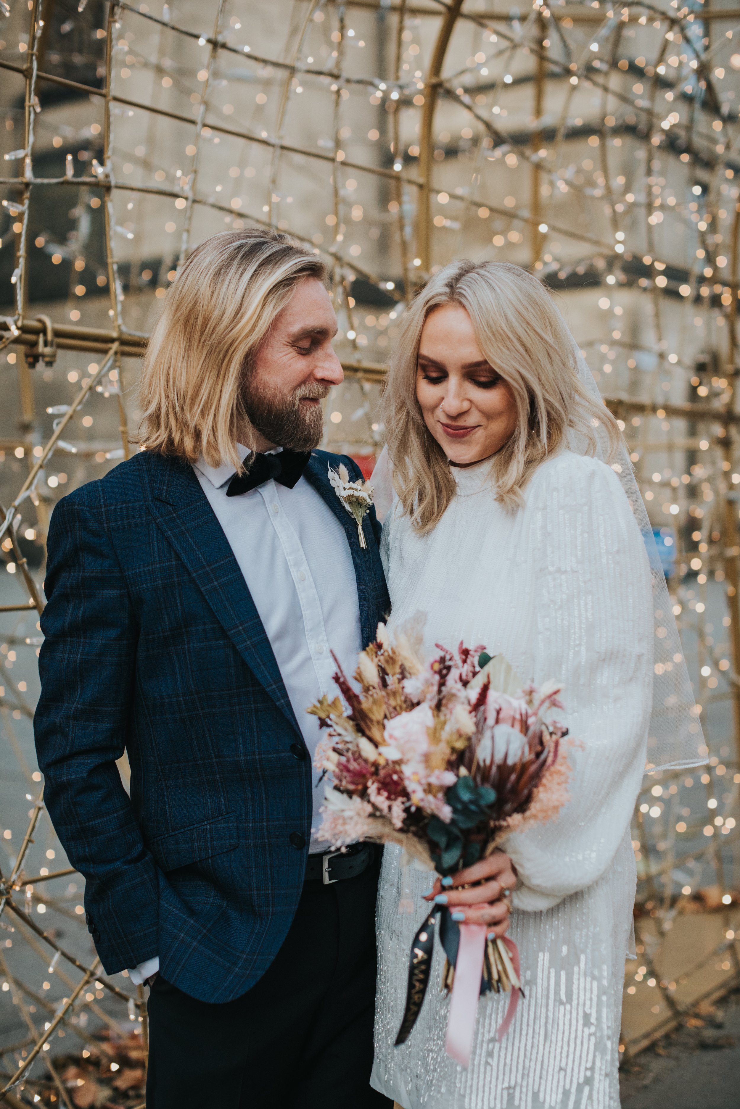 Bride and groom stand together in front of golden Christmas lights.s