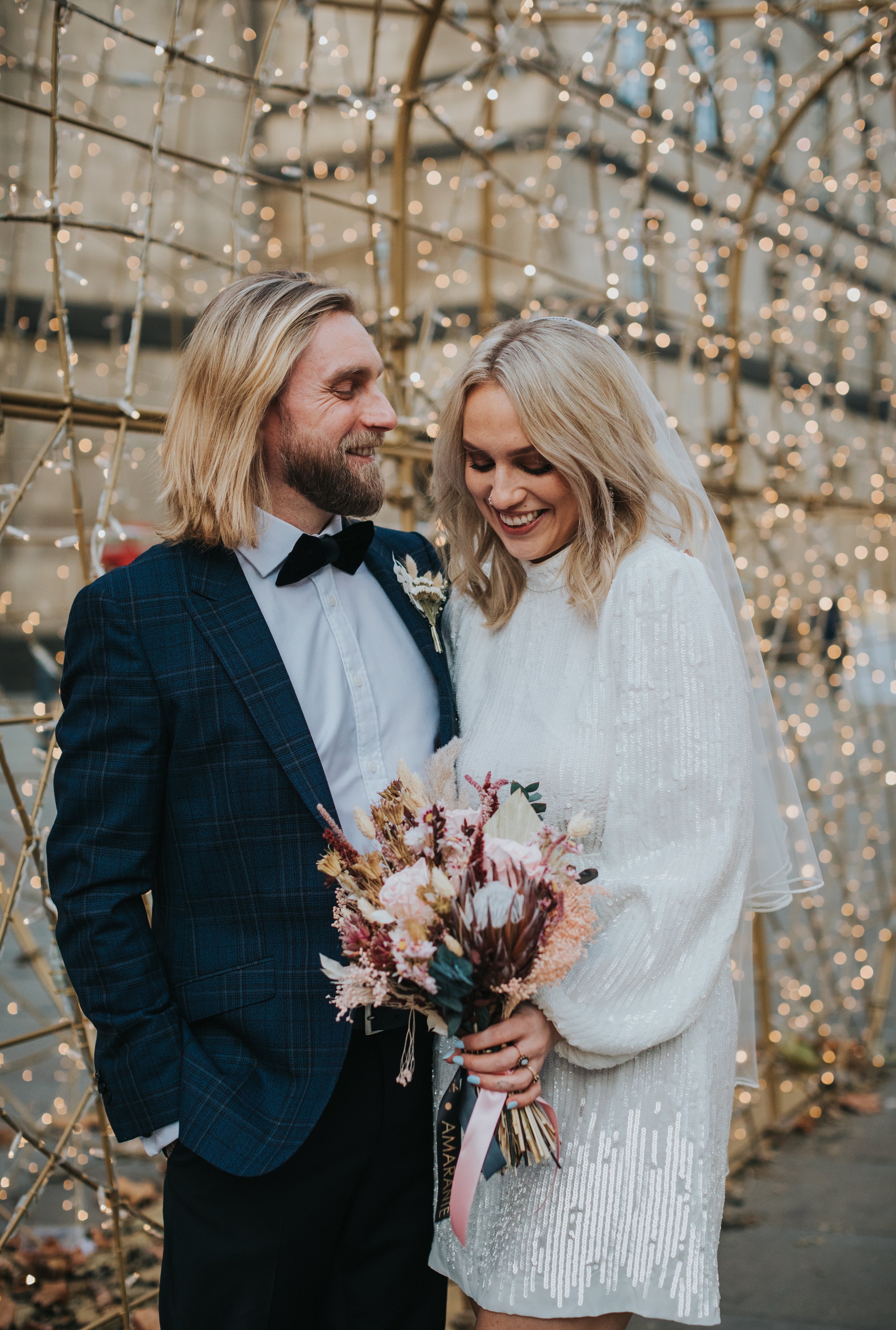 Bride and groom laugh together in front of golden Christmas light bokeh. 