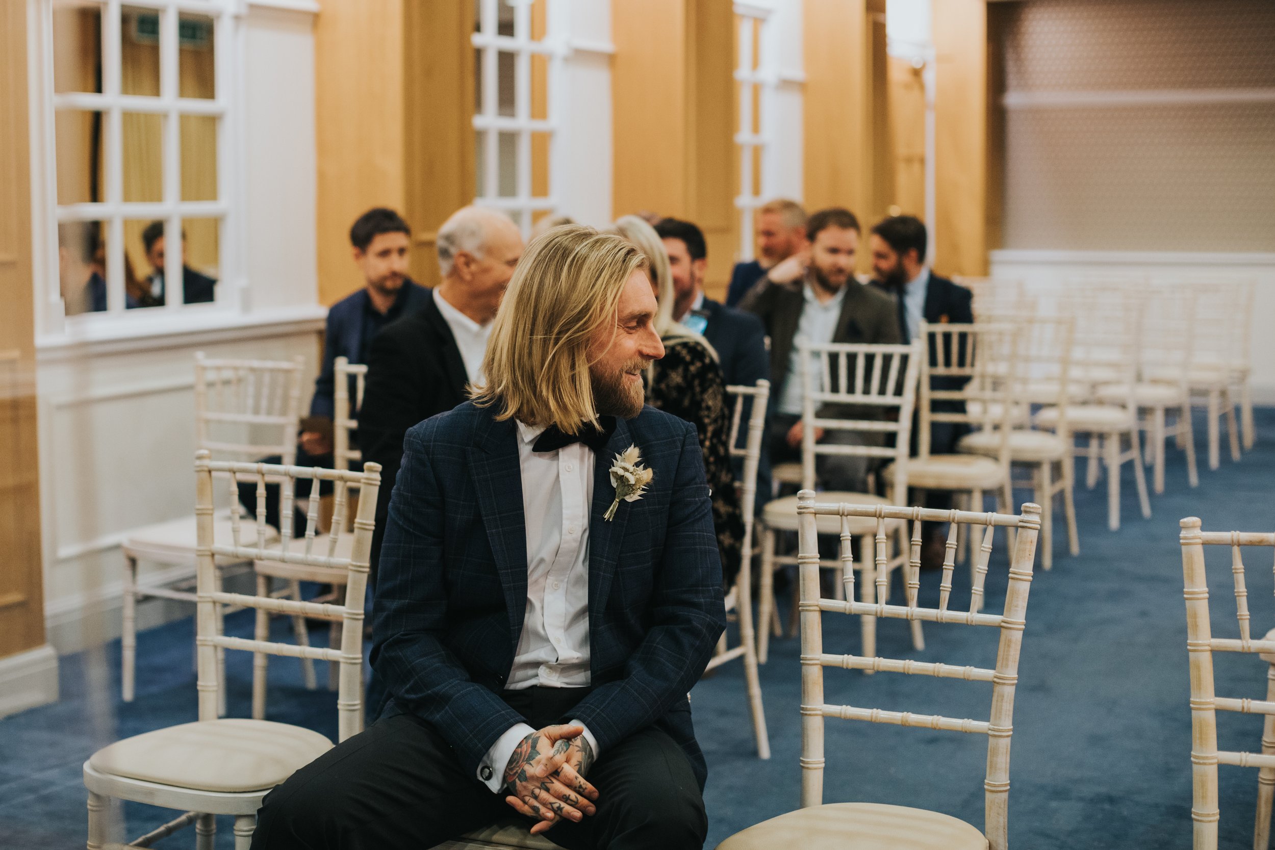 Groom sits in ceremony room waiting for his bride. 