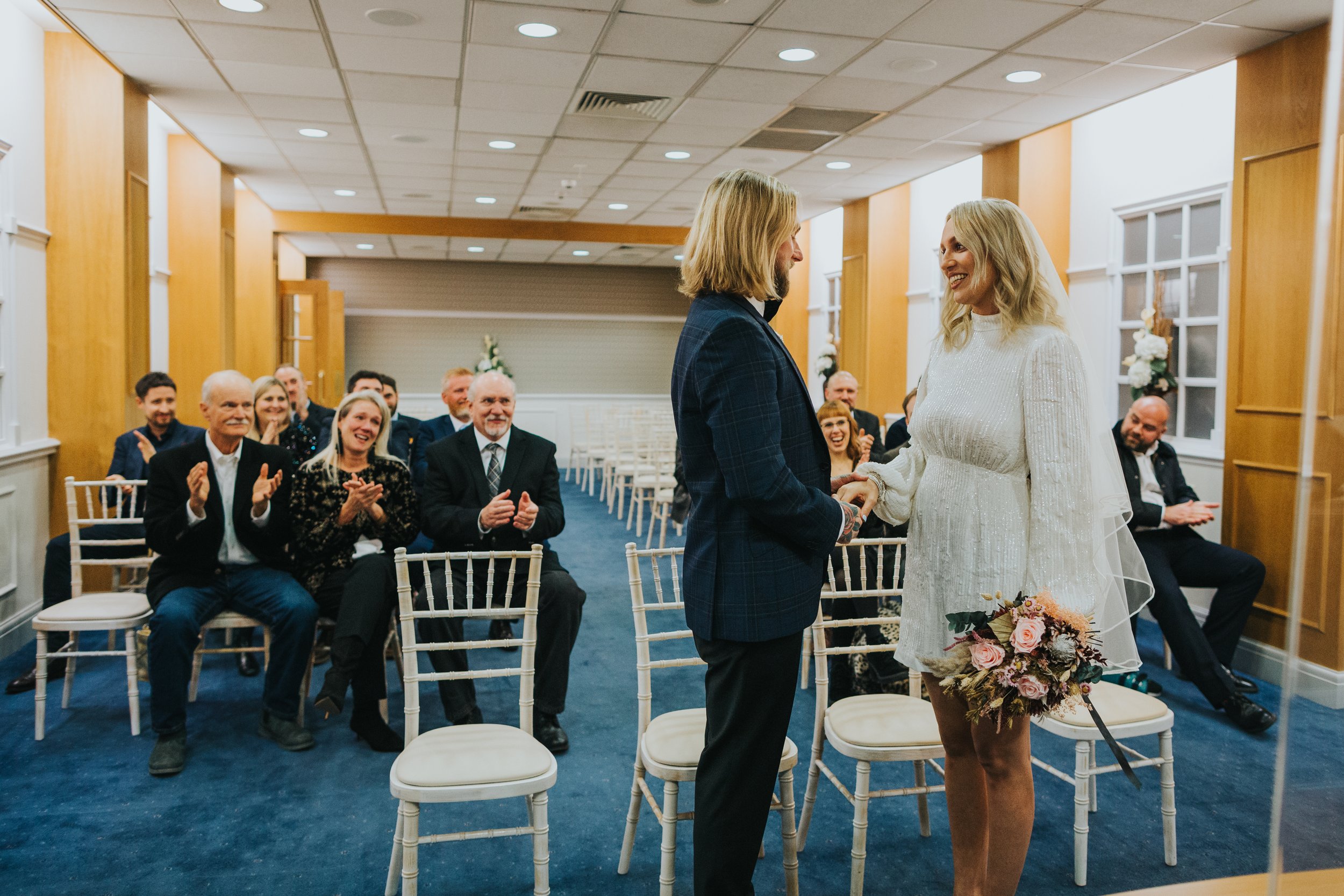  Bride and groom with wedding guests clapping behind them.