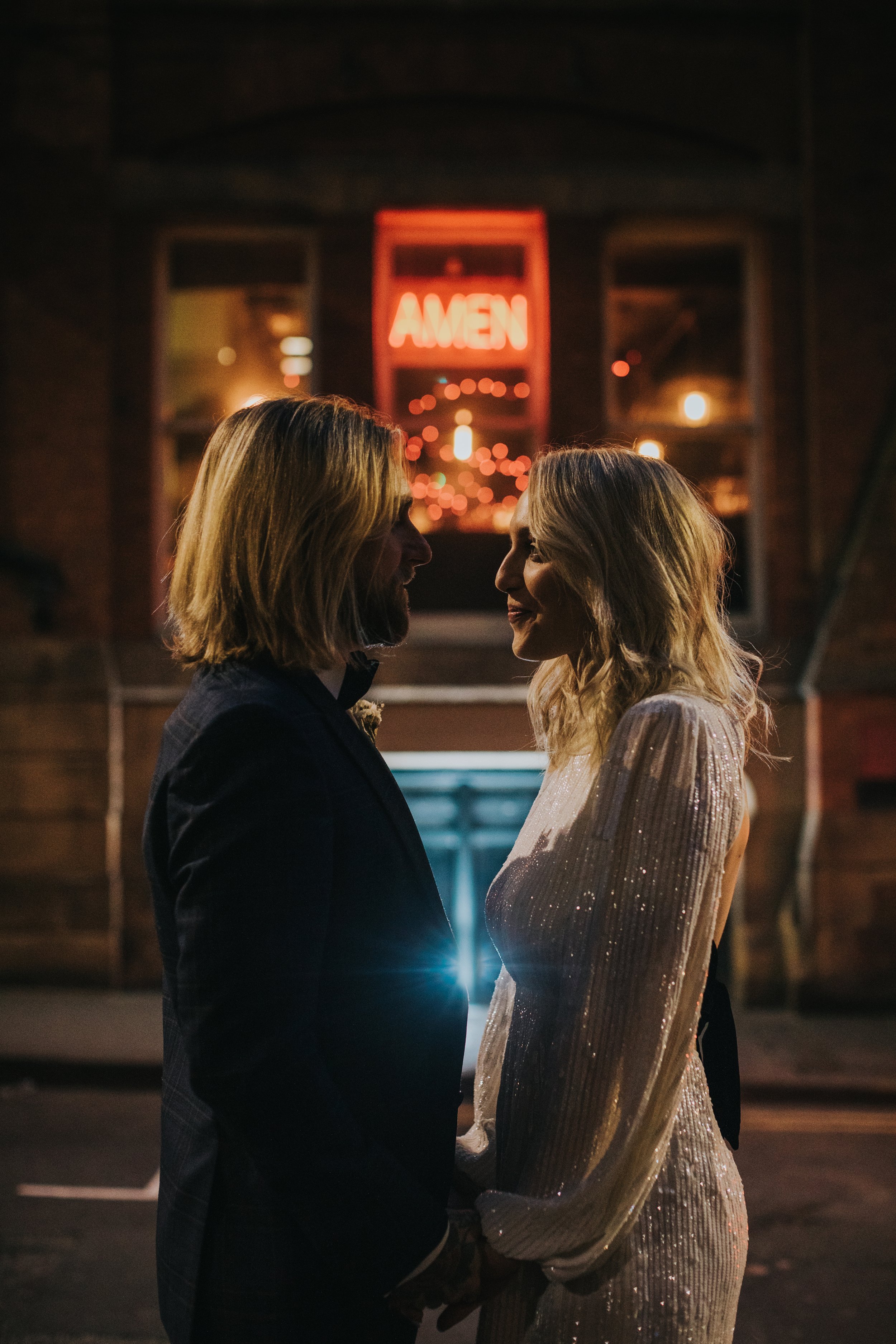 Mid shot of bride and groom in front on Neon "Amen" sign in Manchester City Centre