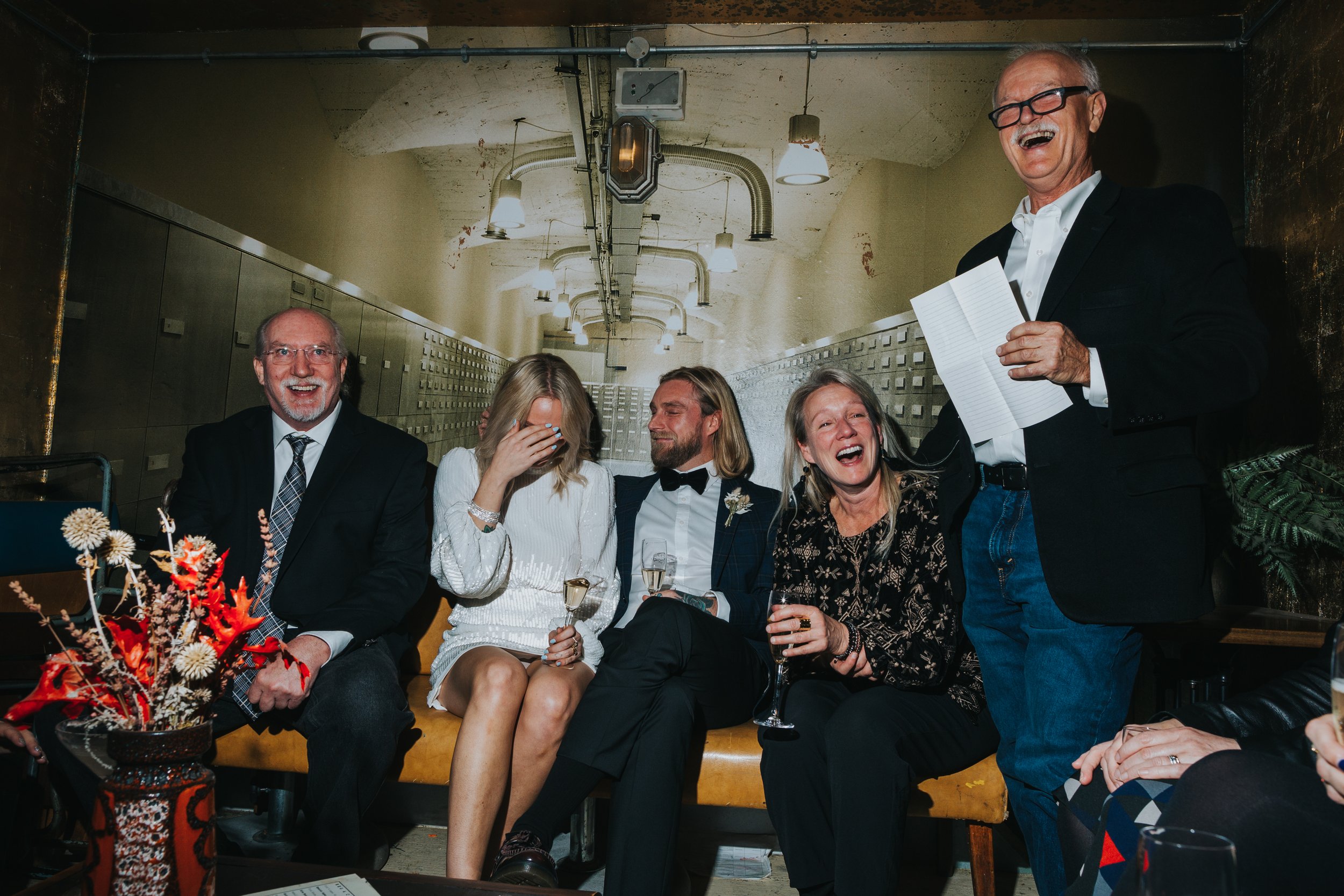 Everyone laughs at step fathers speech as the bride hides her face. 