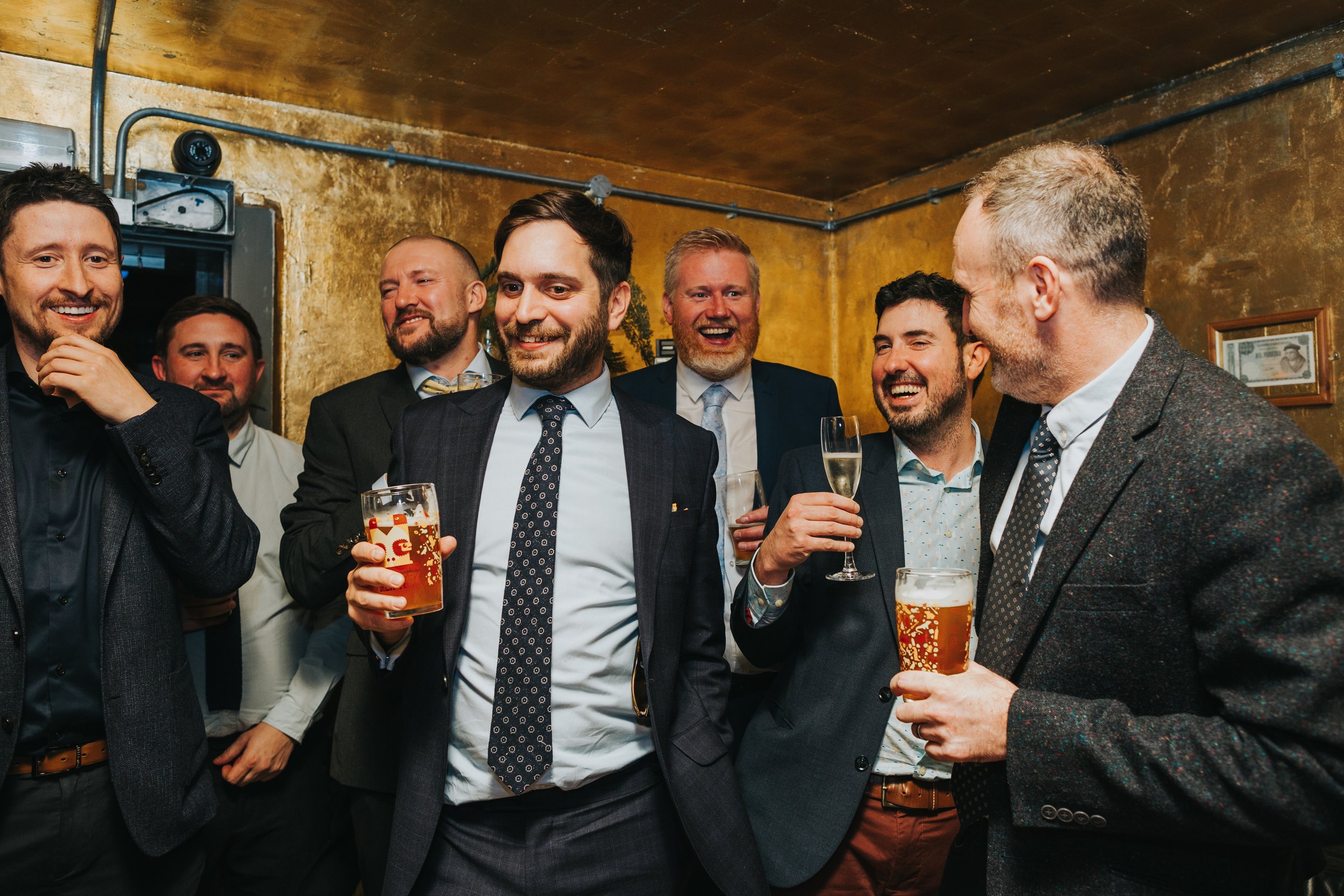 Wedding guests laugh together, drinks in hands. 