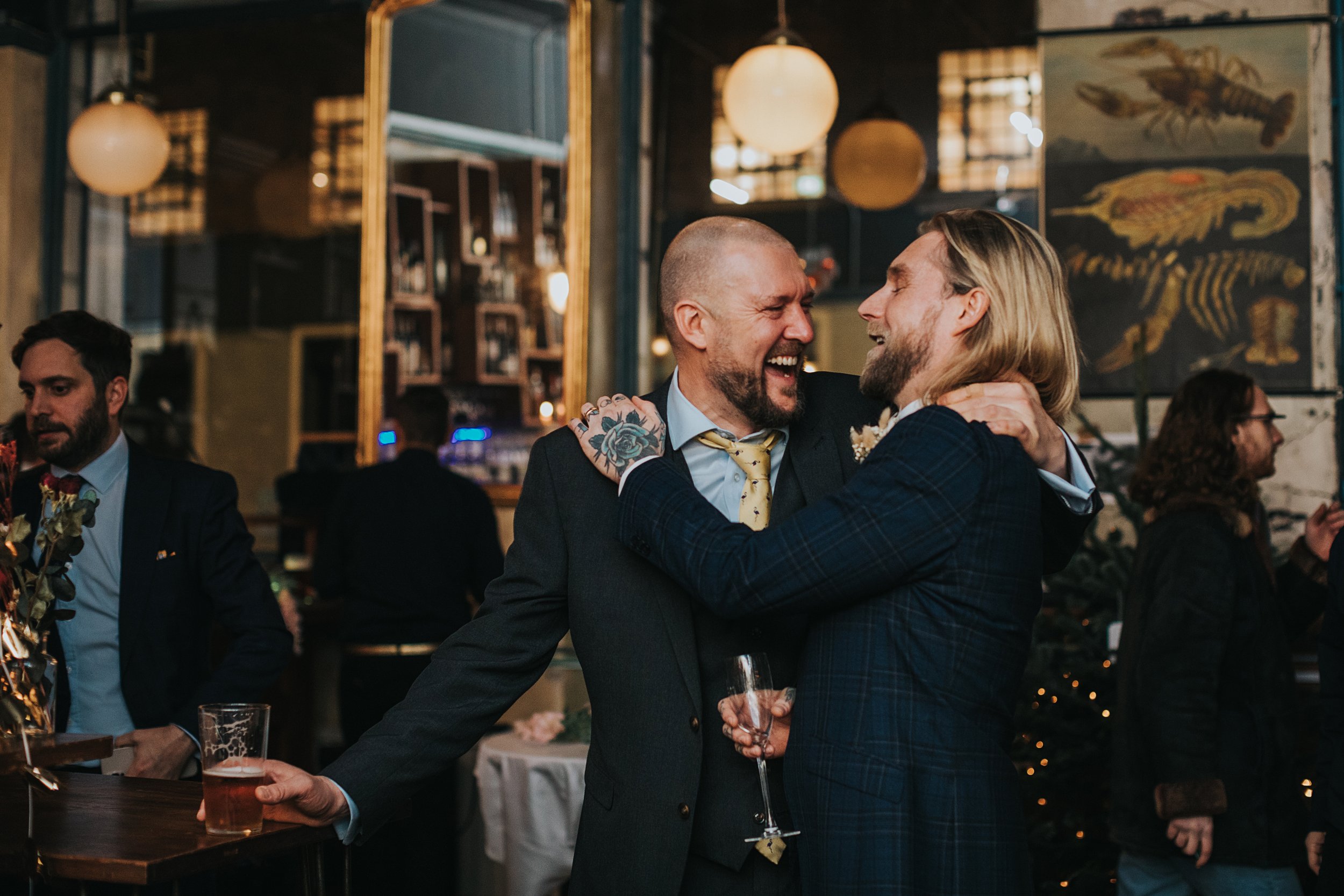 Groom and friend laugh together while hugging. 