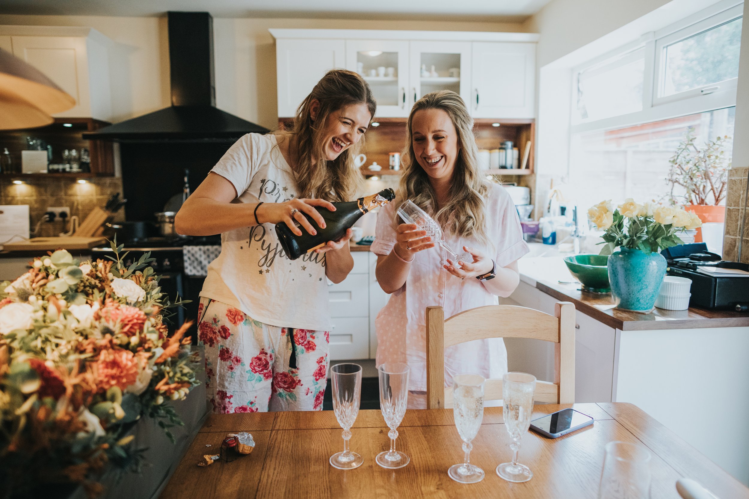 Brides laugh as they pour glasses of Champange for the bridal party