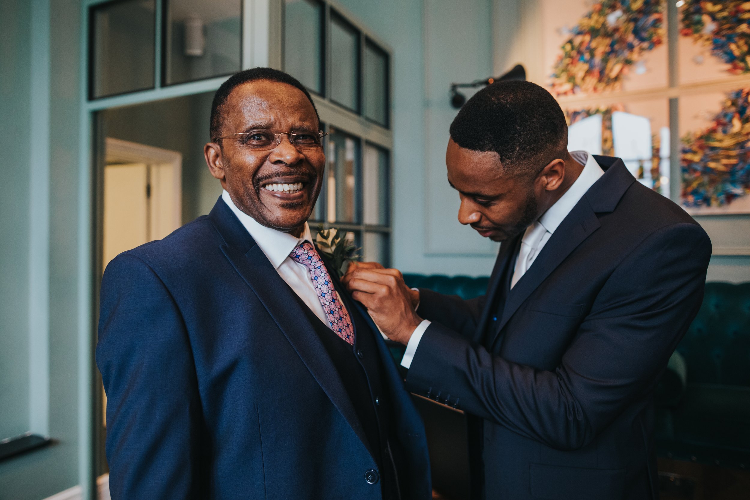 Groom puts button hole flower on his Father's suit. 